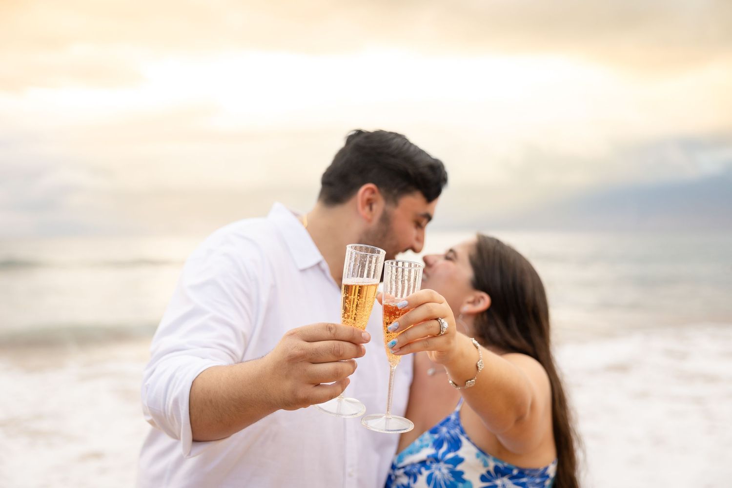 Romantic couple toasting champagne glasses on a beach at sunset during Hawaii vacation.