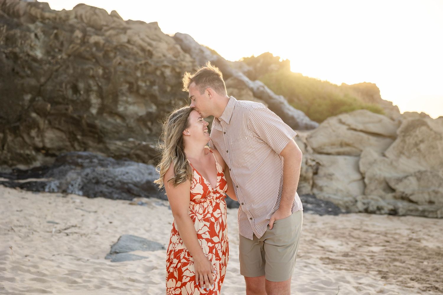 Couple sharing a tender kiss on a sandy beach at sunset.