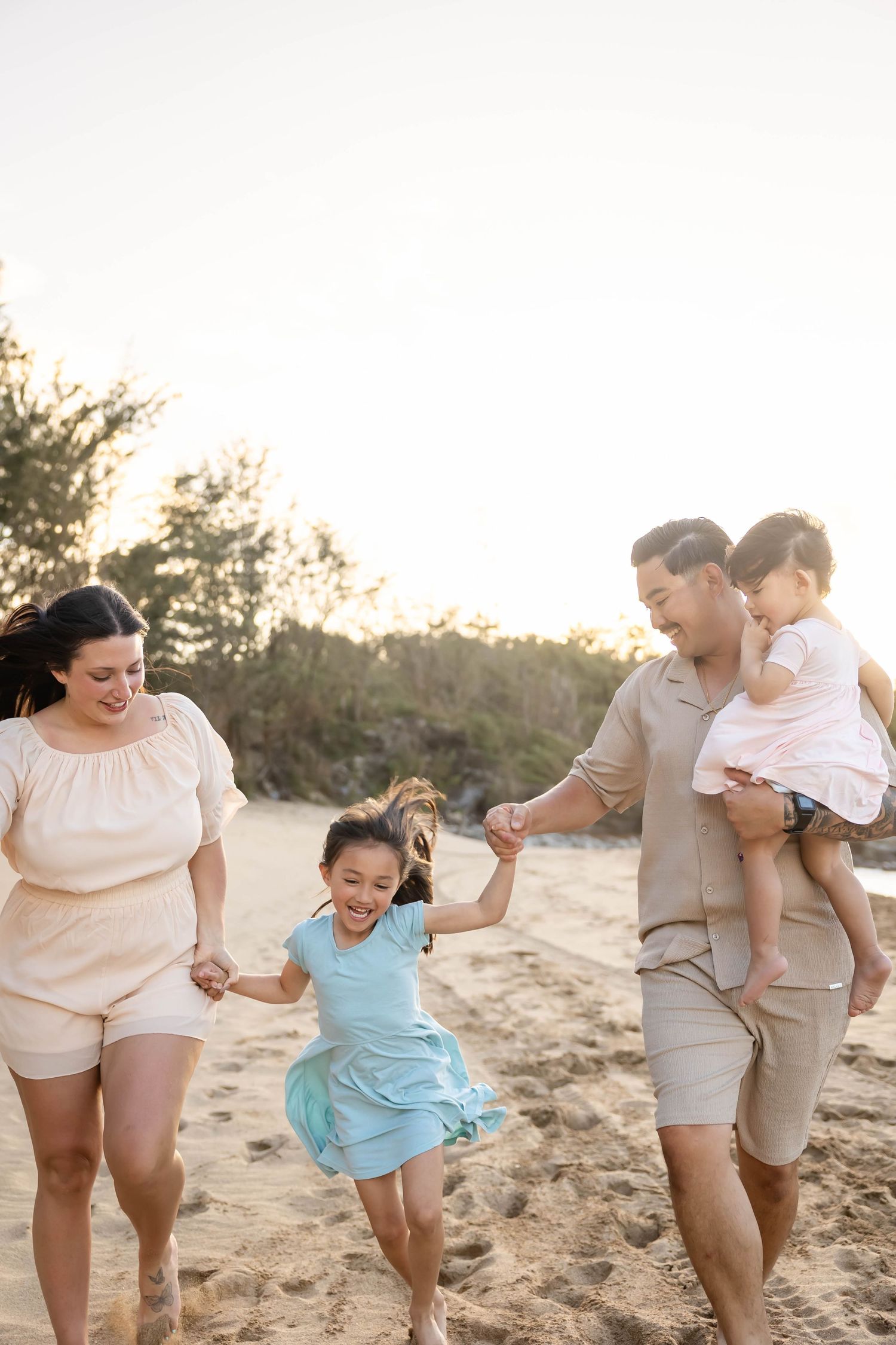 Happy family walking and playing together on a sunny beach, parents holding children's hands.