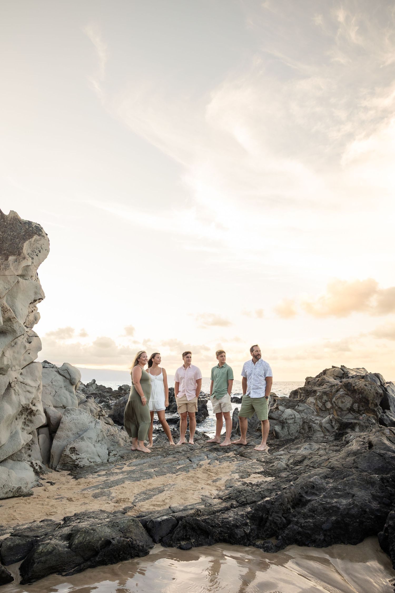 Group of four adults standing on volcanic rocks at a Hawaii beach during sunset.