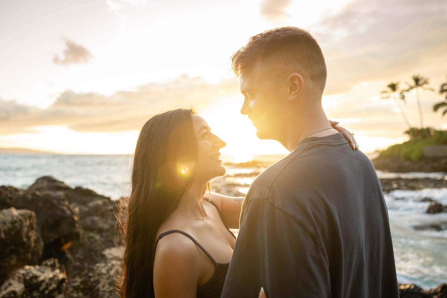 Romantic couple gazing into each other eyes at sunset on Hawaiian rocky coast.