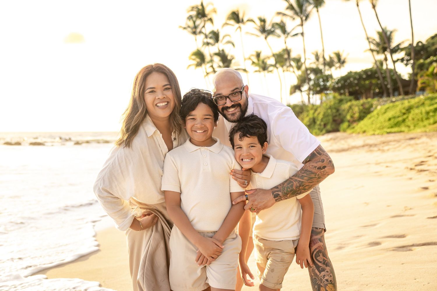 Family of four smiling together on a golden sandy Hawaii beach at sunset.