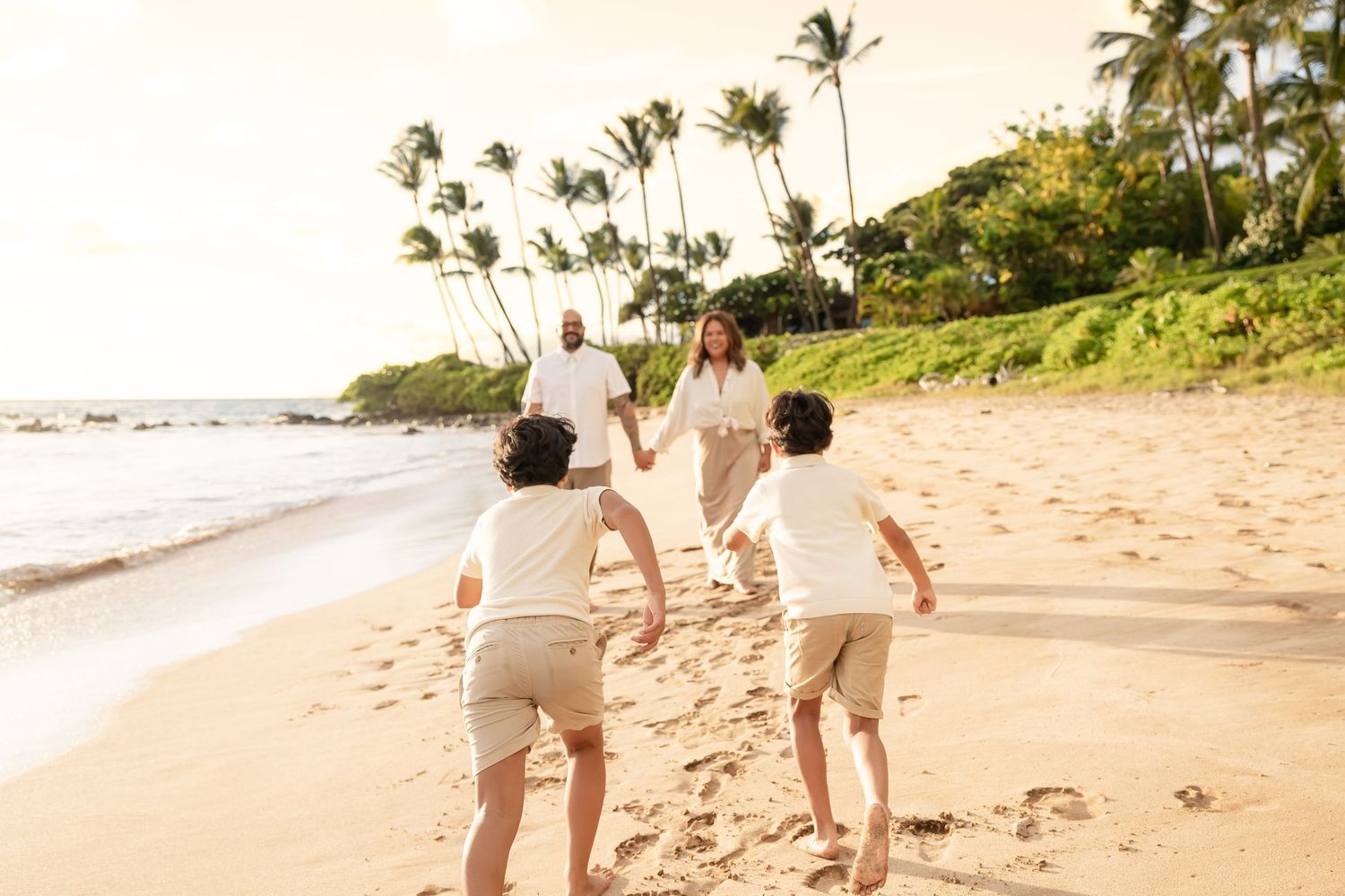 Family running together on a sandy Hawaii beach with palm trees at sunset.