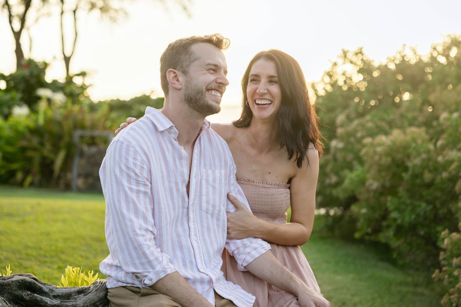 Joyful couple sitting together laughing in a sunlit tropical garden with warm golden light.