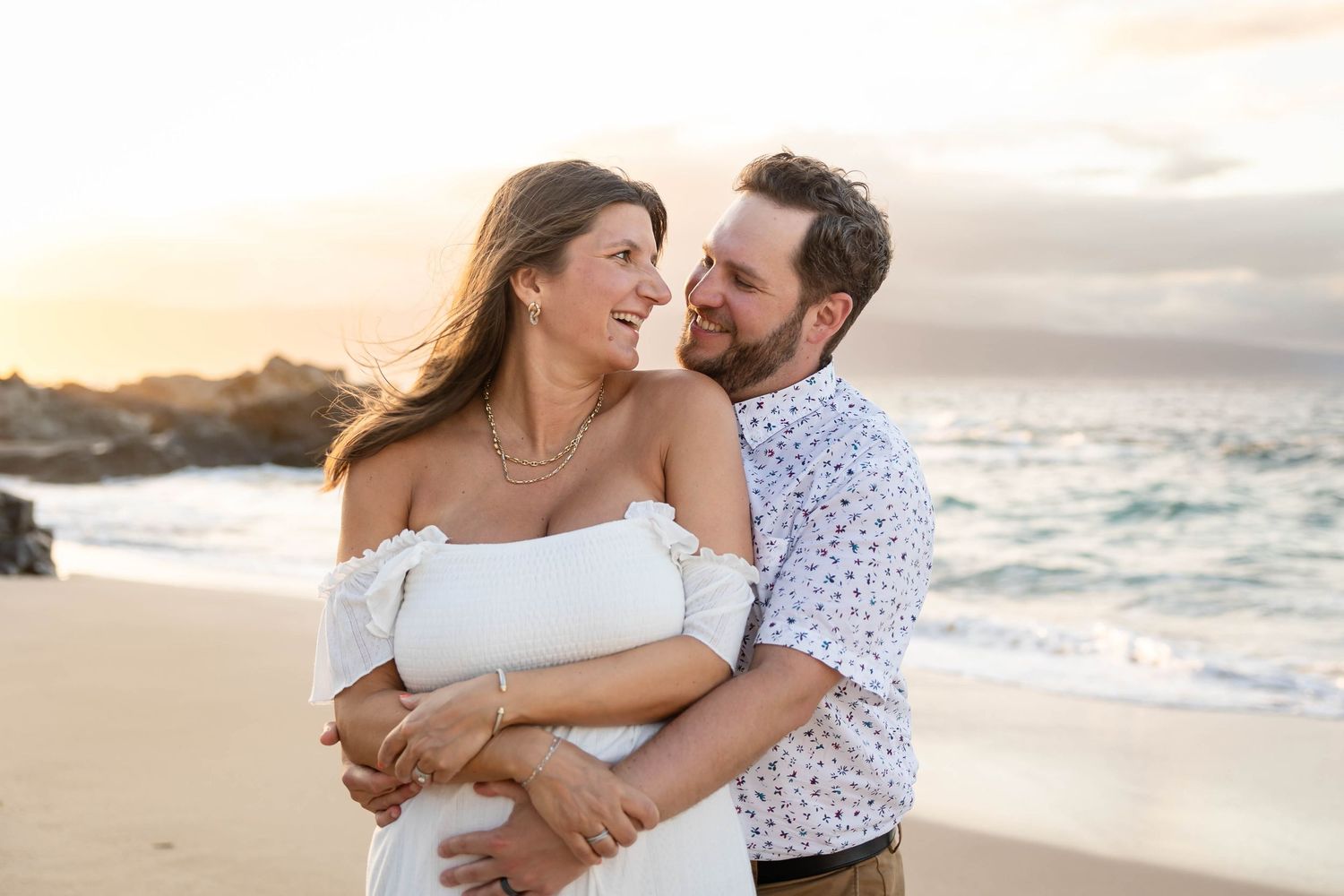 Happy couple embracing and smiling together on a Hawaiian beach at dusk.