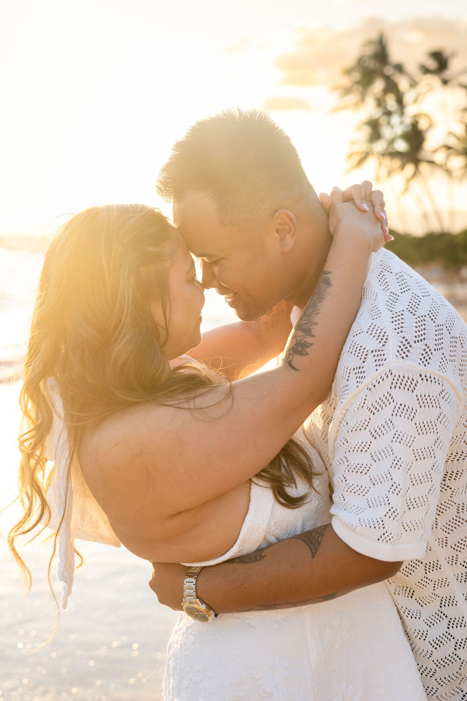 Romantic couple embracing forehead-to-forehead on a beach bathed in warm golden sunset light.