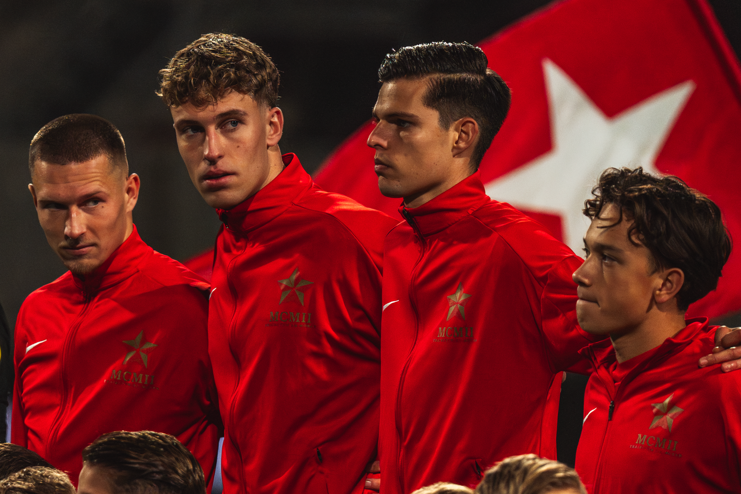 Soccer players in bright red team uniforms stand together before a match against a dark background.
