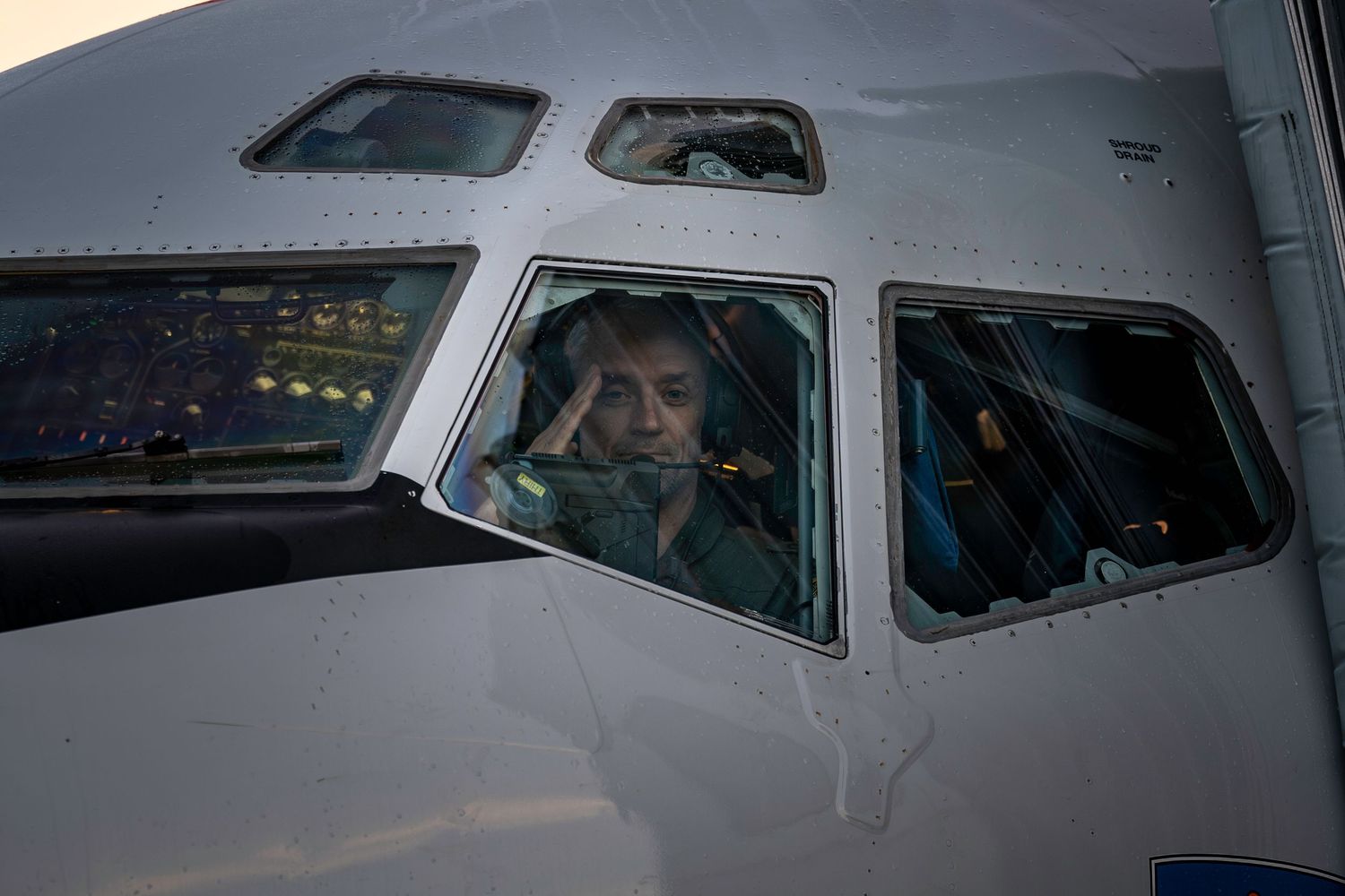 Cockpit view through the NATO AWACS E-3A aircraft window showing a pilot saluting the photographer.