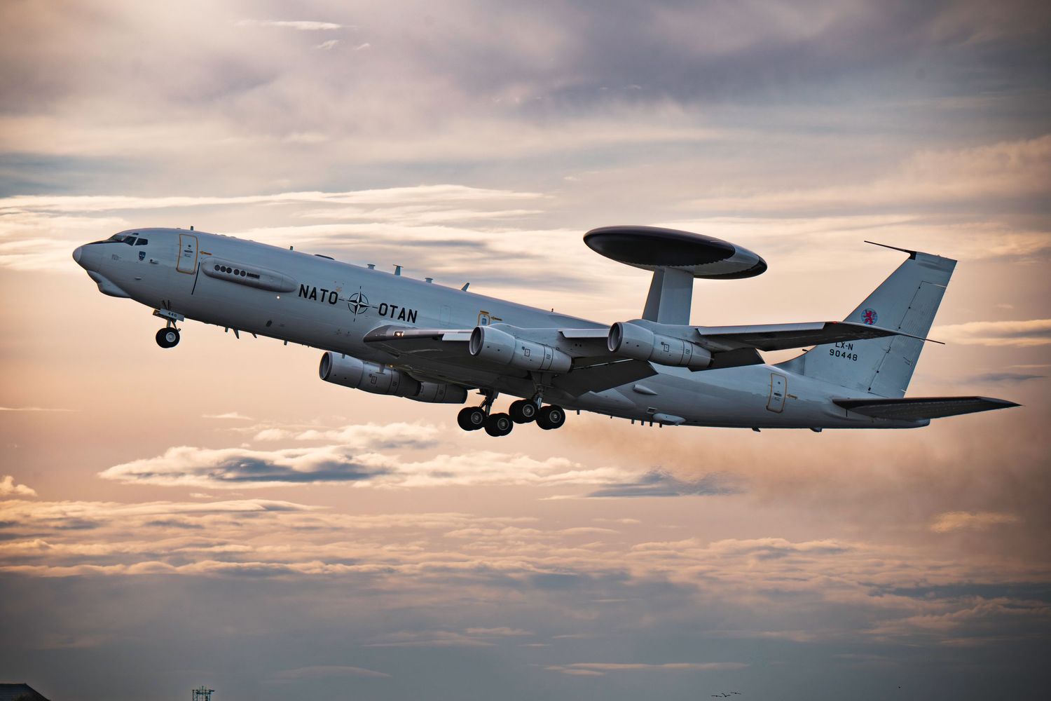 NATO AWACS E-3A Sentry surveillance aircraft flying against dramatic sunset sky with orange clouds.