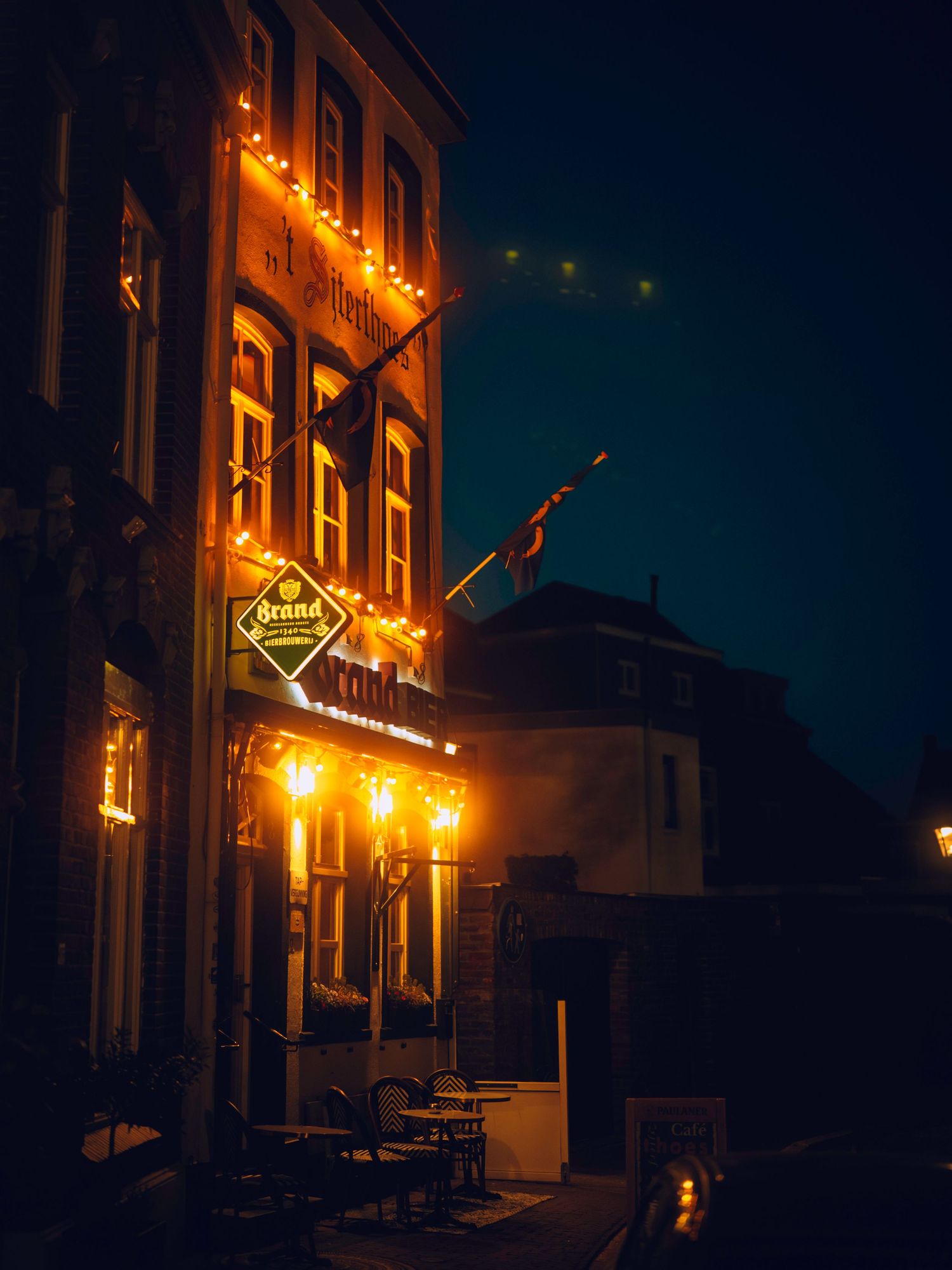 A dimly lit street at night with warm glowing storefront signs and windows creating a moody urban atmosphere.