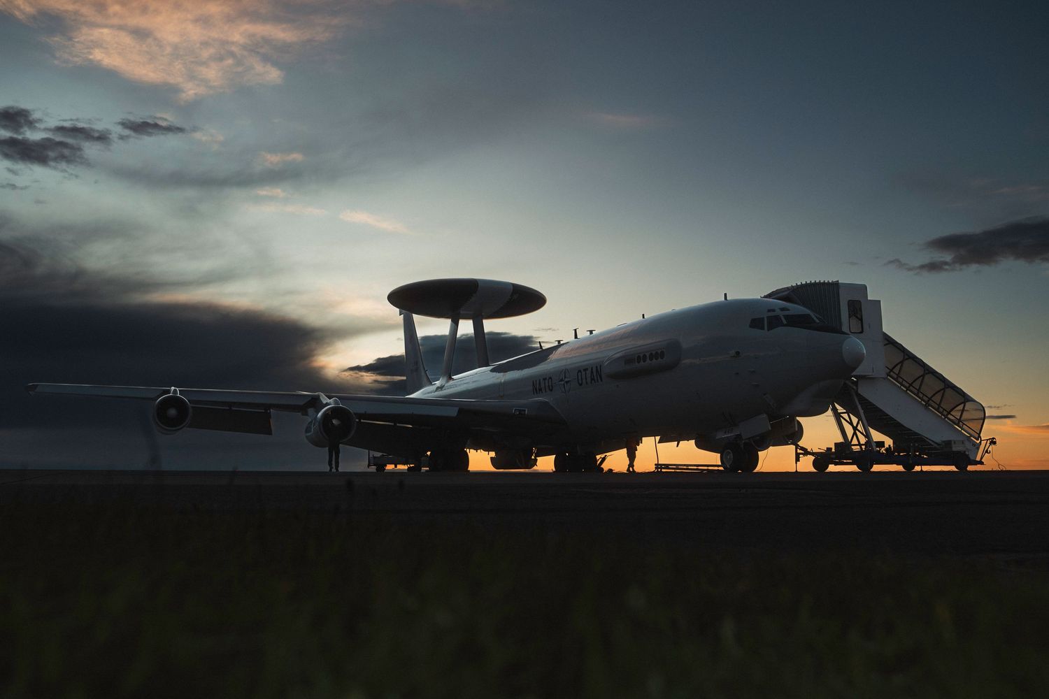 A silhouette of an E-3A aircraft against a dramatic sunset sky with orange and purple hues.