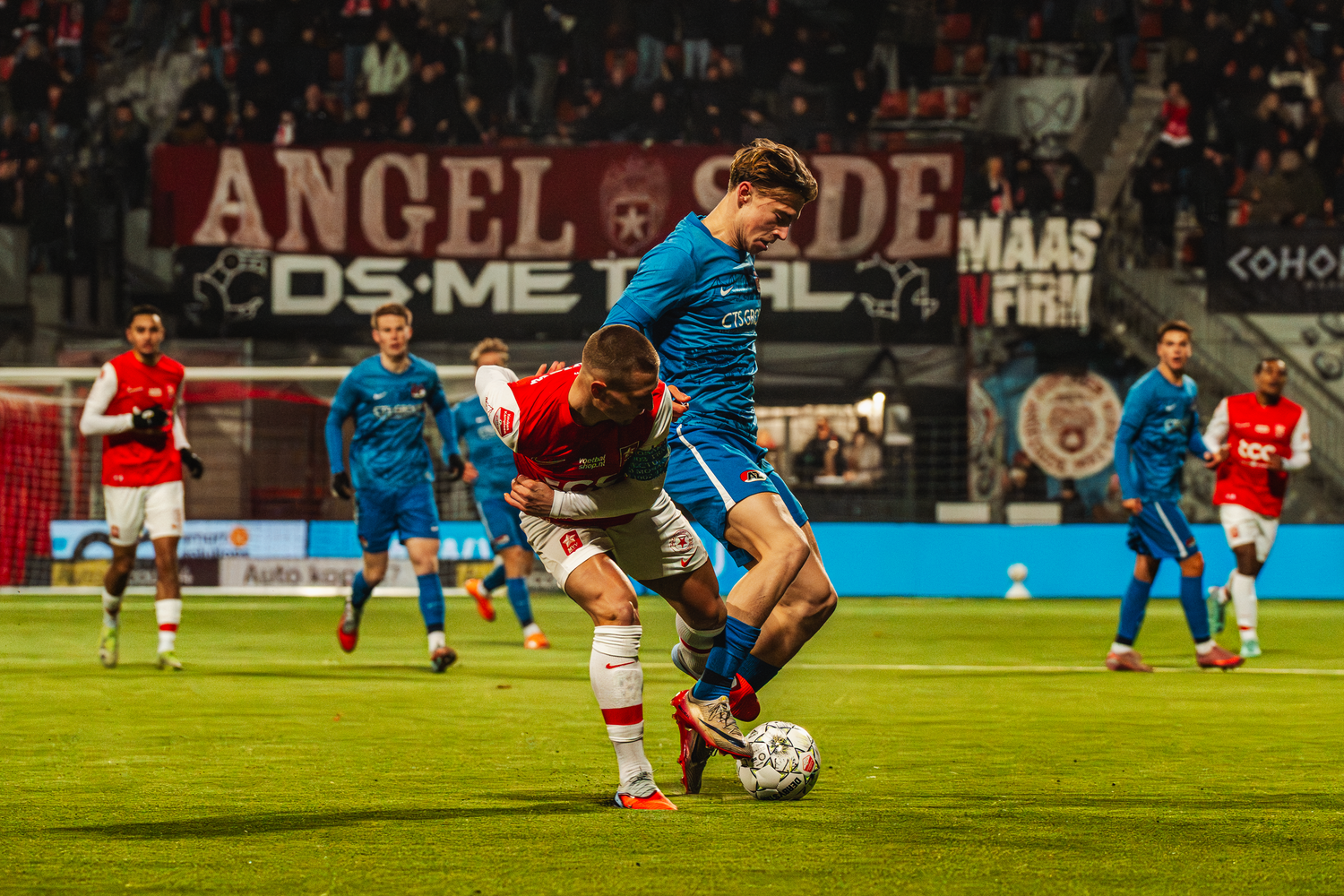 Soccer players compete for possession of the ball during an intense match on a floodlit stadium field.