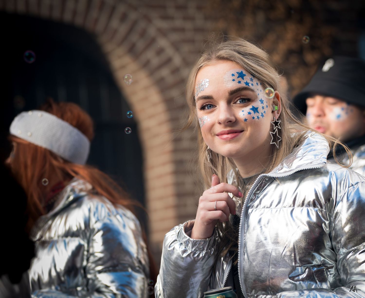 Outdoor portrait of a woman wearing a silver jacket and face paint, photographed during an event.