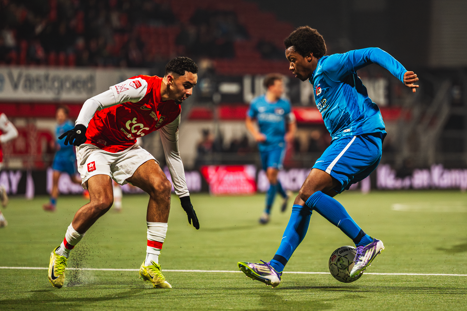 Soccer players in red and blue uniforms compete for possession of the ball during an intense match.