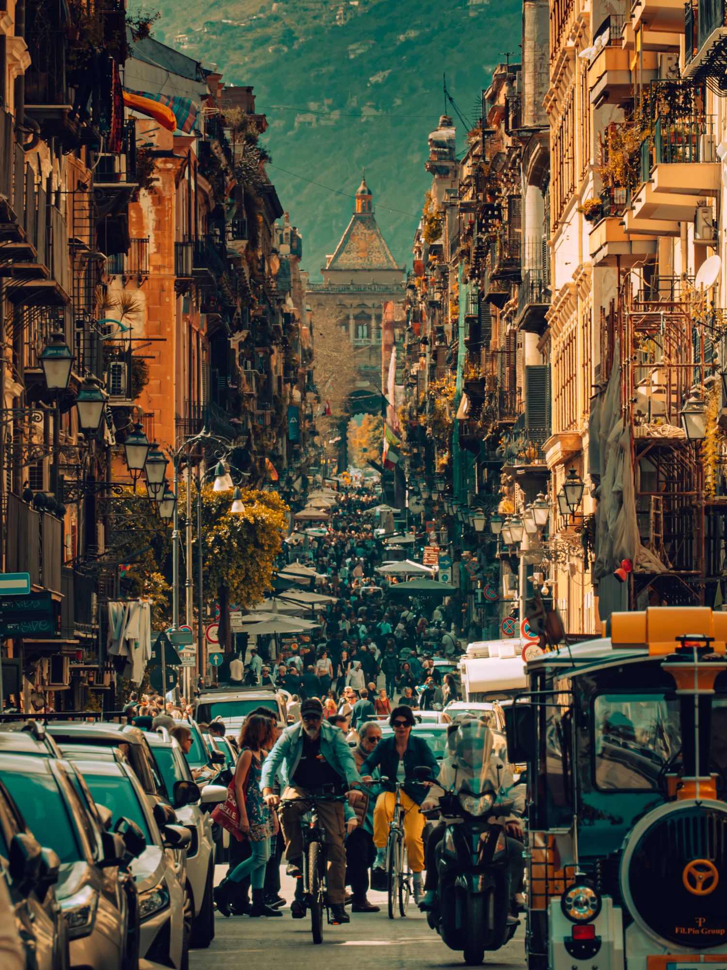 Busy street scene in Palermo, Sicily with vintage buildings and parked cars under a dramatic turquoise sky.