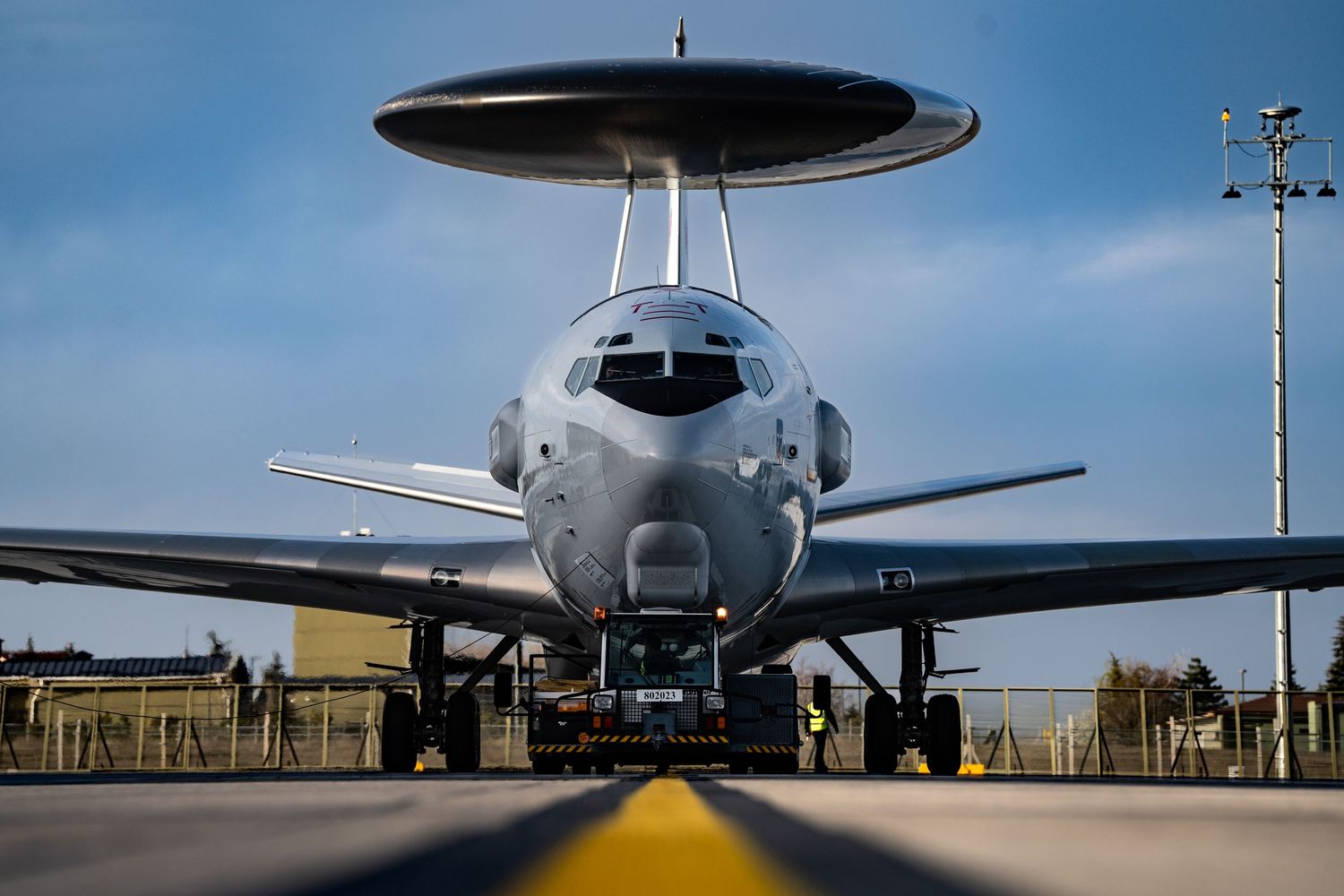 Military surveillance aircraft, a NATO AWACS E-3A on runway with its distinctive radar visible against blue sky.