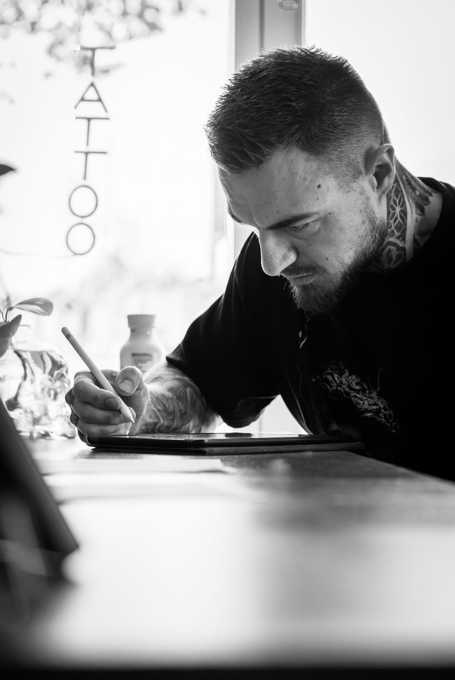 Black-and-white photograph of a tattoo artist sketching at a work table.