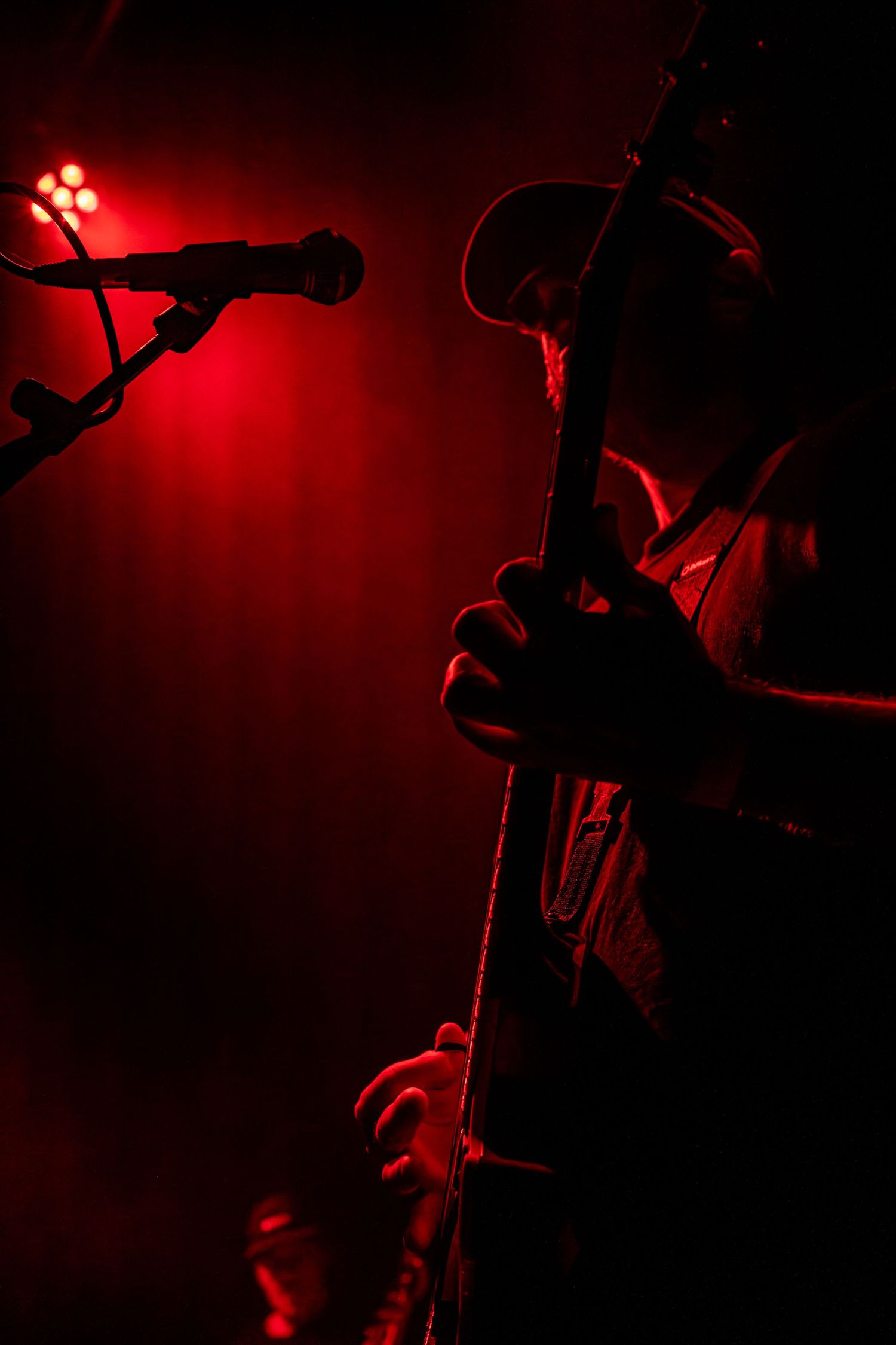 Silhouetted figures perform on a dark stage illuminated by dramatic red lighting creating a moody atmosphere.