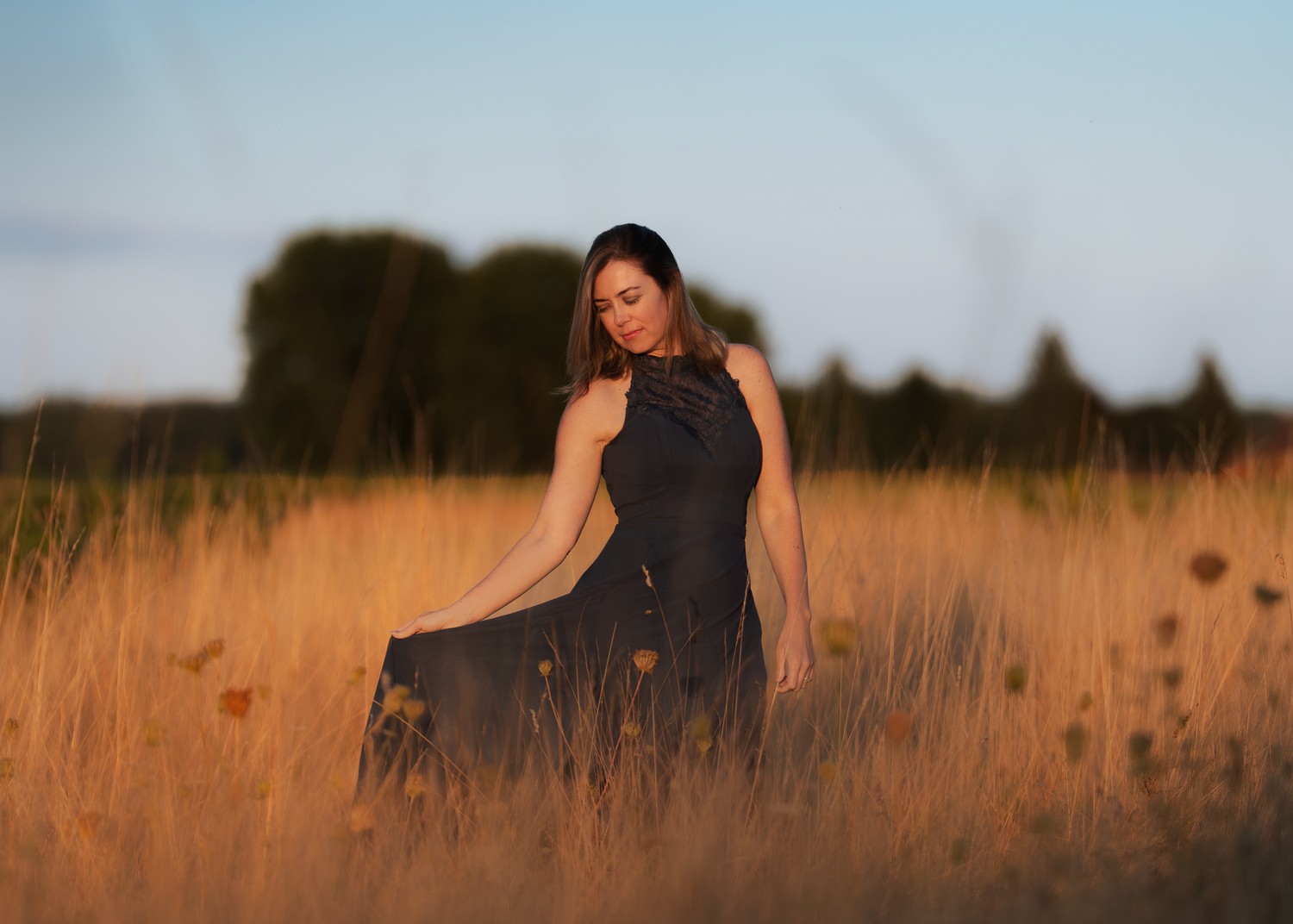 A person in a navy dress stands in a golden wheat field at sunset, creating a silhouetted profile.