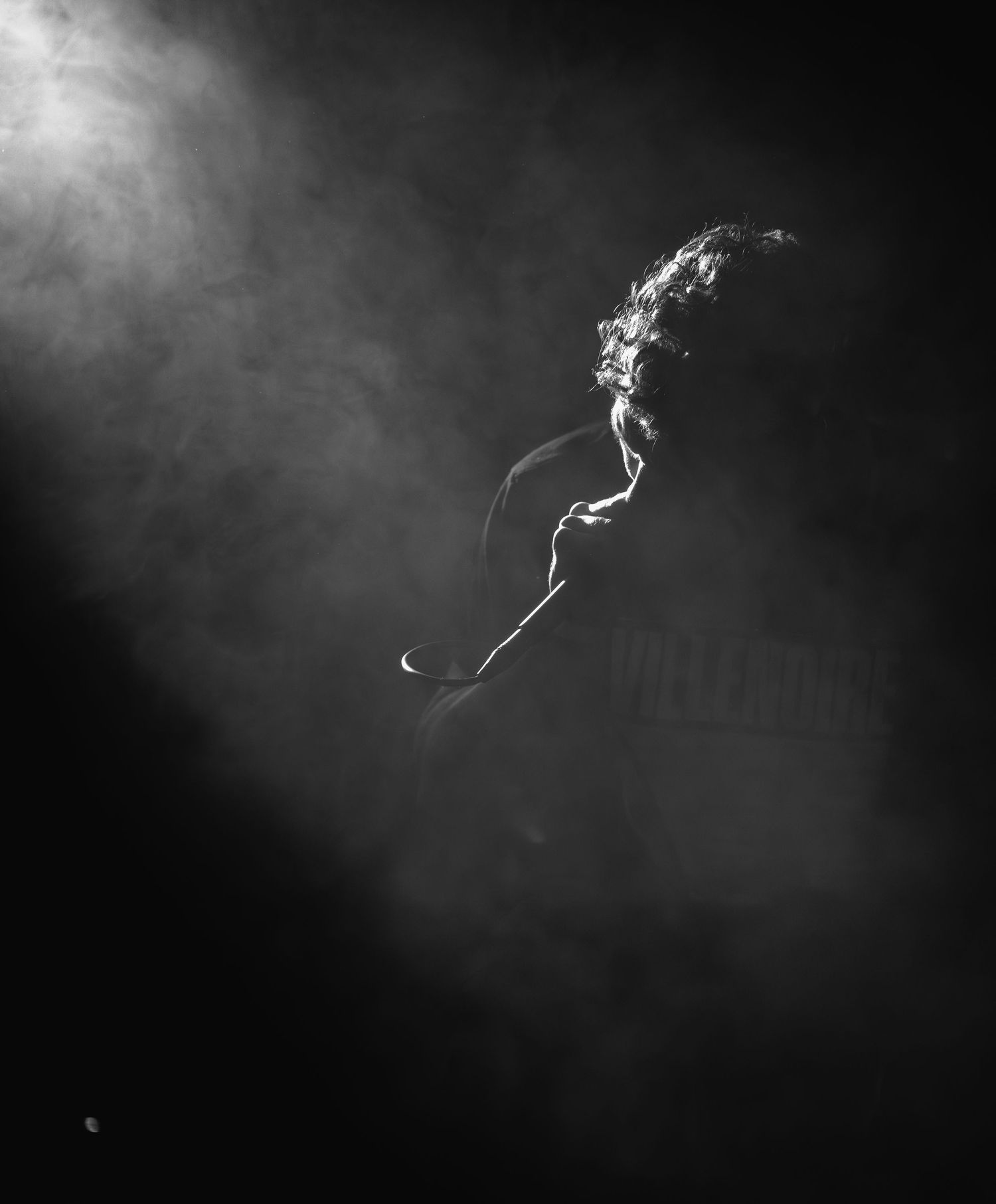 Smoke wisps floating and curling against a dark background as a hardcore band singer screams into his microphone during a live show.