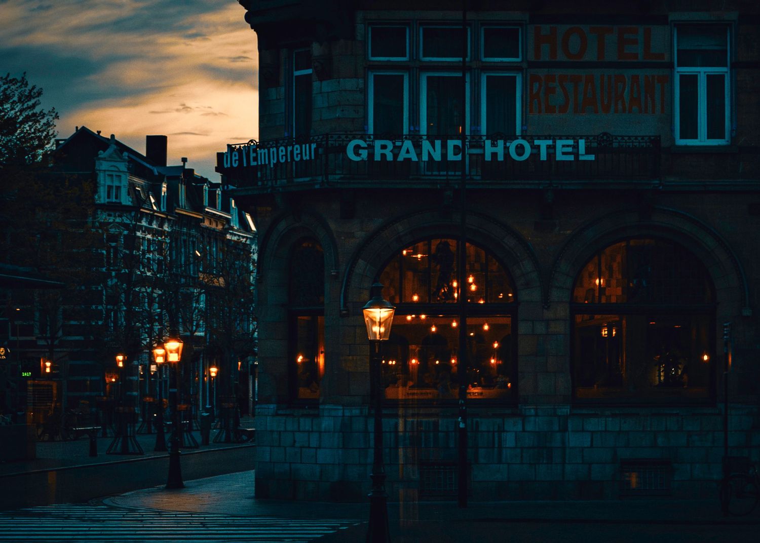 Historic Grand Hotel illuminated at dusk with warm glowing street lamps and arched windows against a moody evening sky.