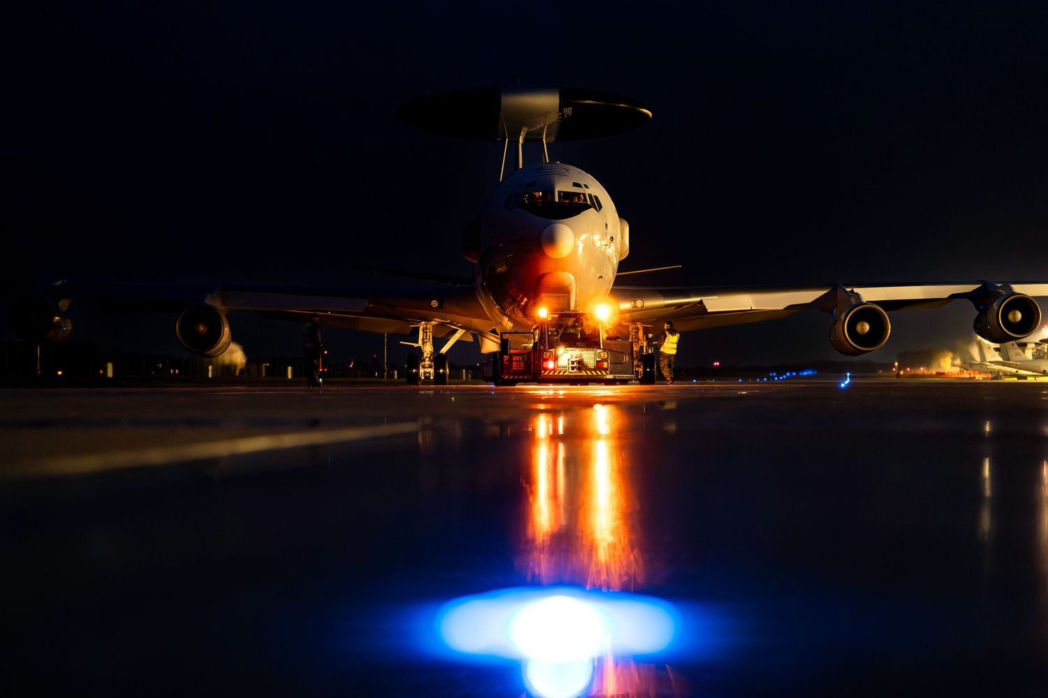 Aircraft landing lights illuminate the dark runway with bright blue and orange glows during nighttime operations.