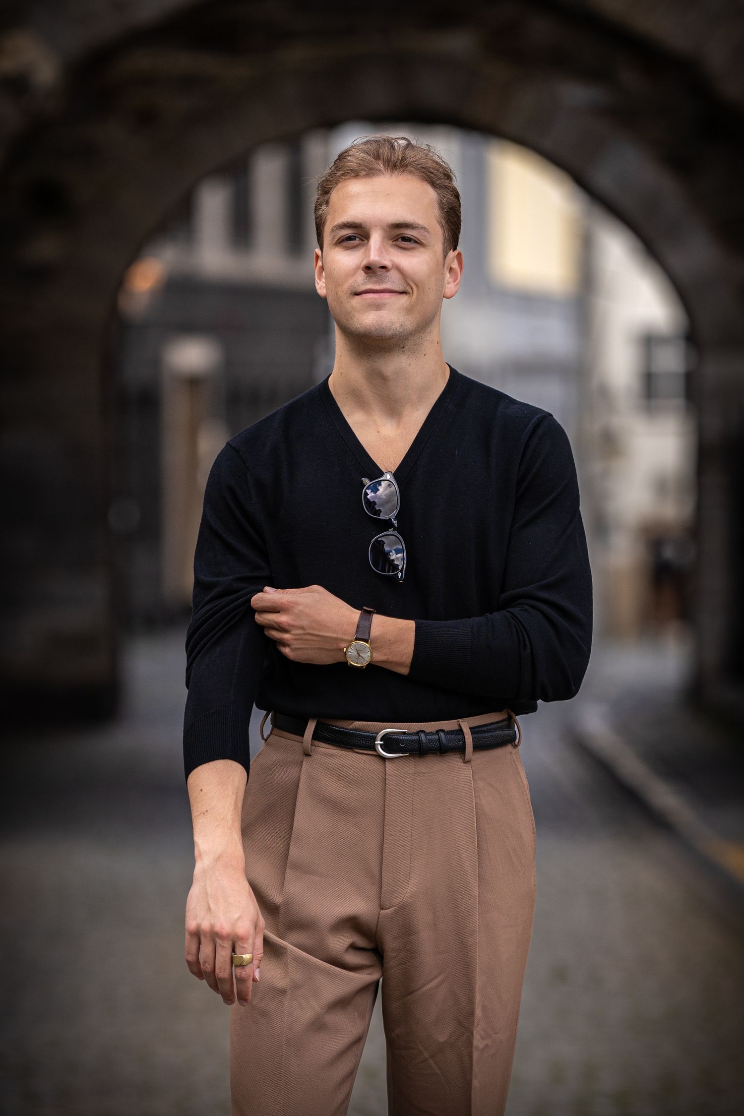A series of fashion portraits showing a man wearing a black v-neck top with tan trousers in an urban setting.