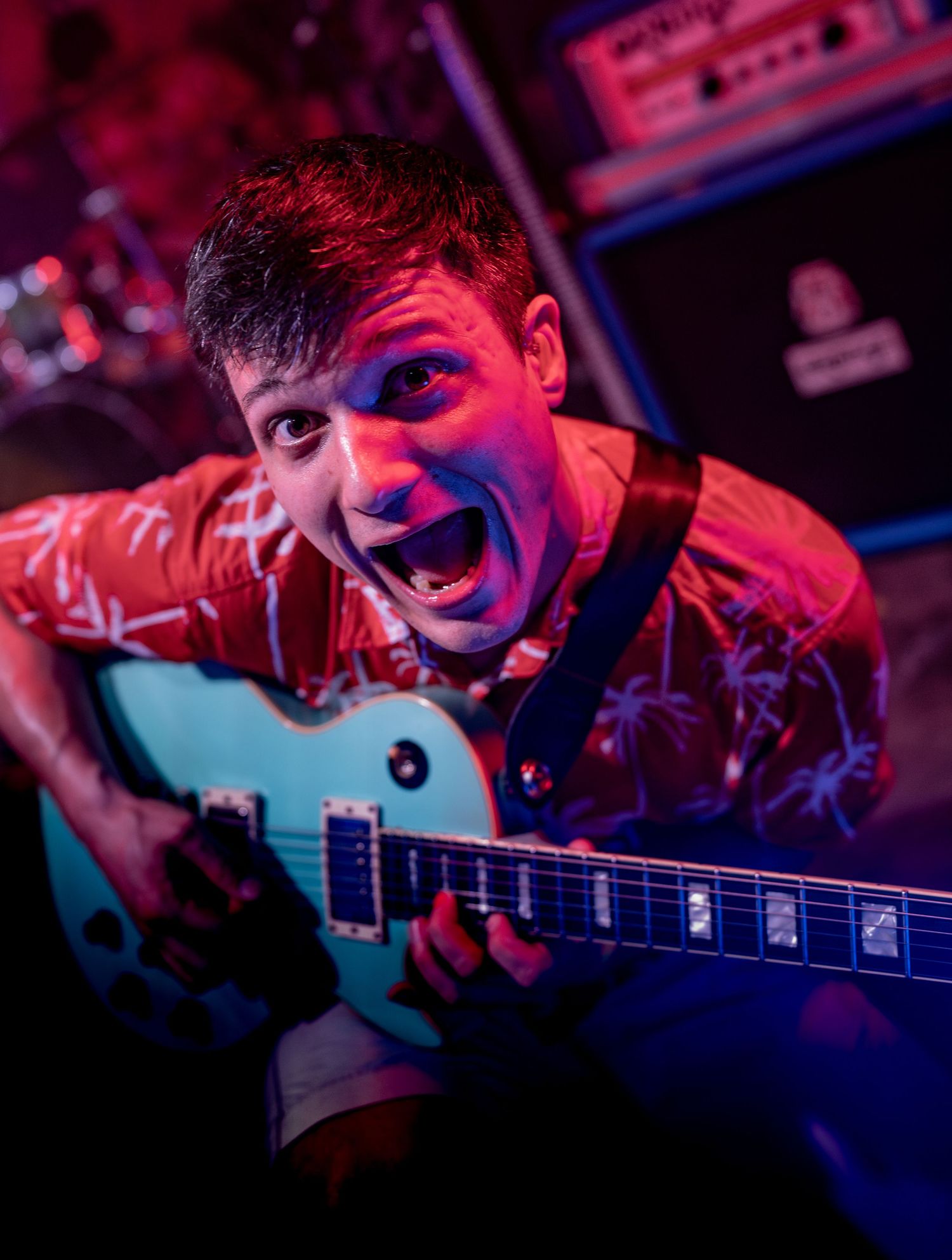 Energetic musician performs with electric guitar under dramatic red and blue stage lighting at a live concert venue.