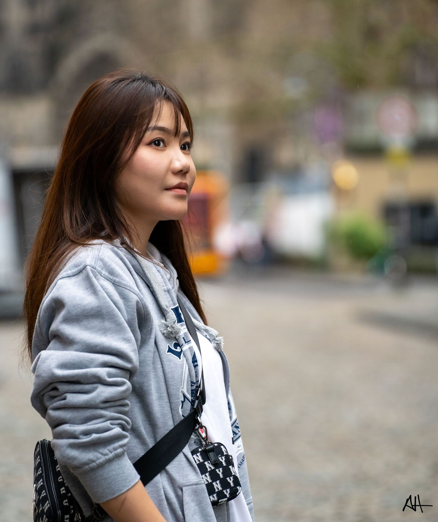 Street-style portrait of a woman wearing a grey sweatshirt, photographed outdoors in an urban setting.