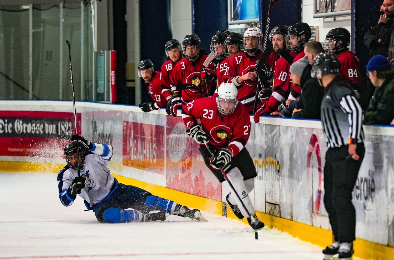 Hockey players compete on ice during an intense game as teammates watch from the bench