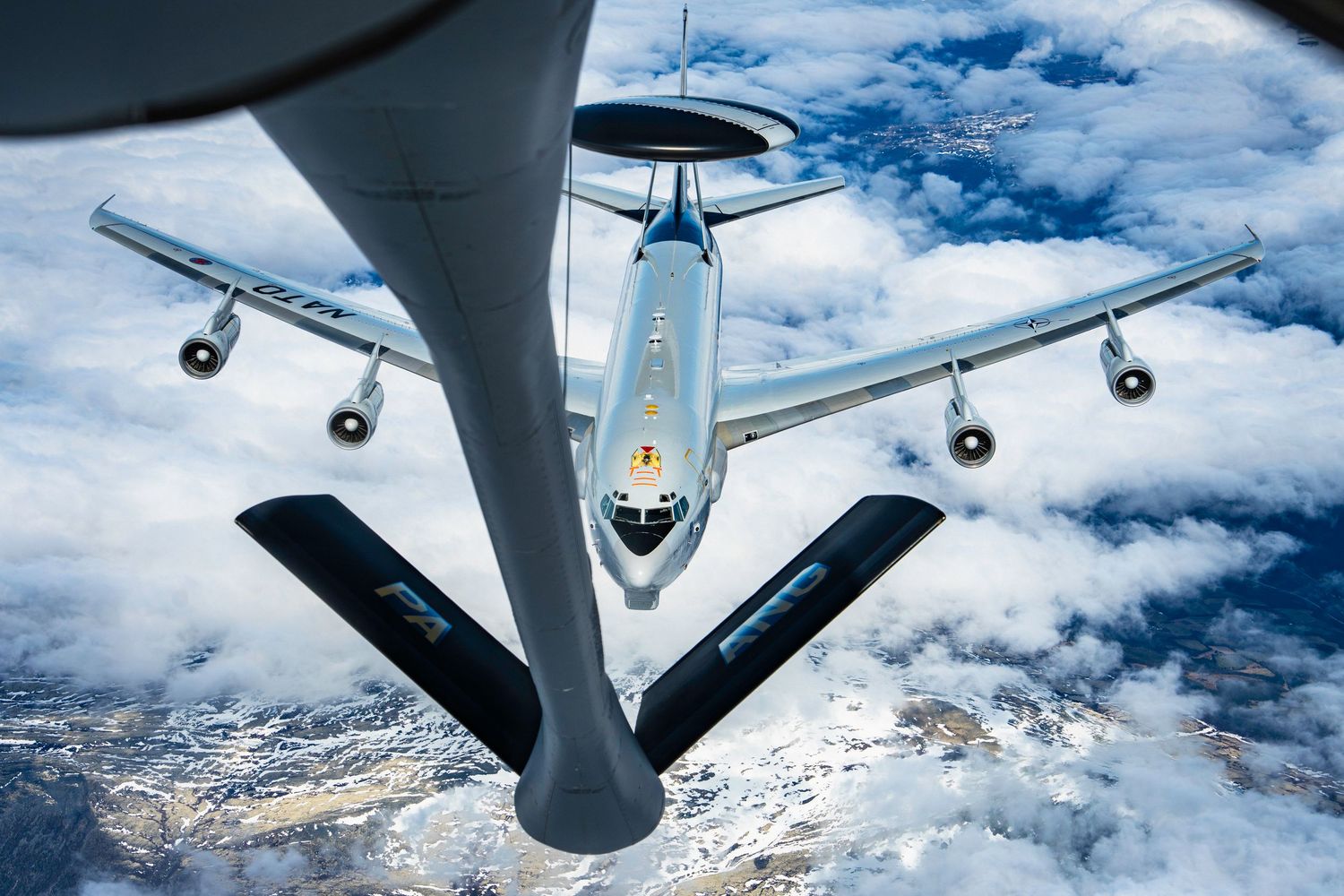 Military aerial refueling operation with KC-135 Stratotanker extending fuel boom to receiving aircraft over snow-capped mountains.
