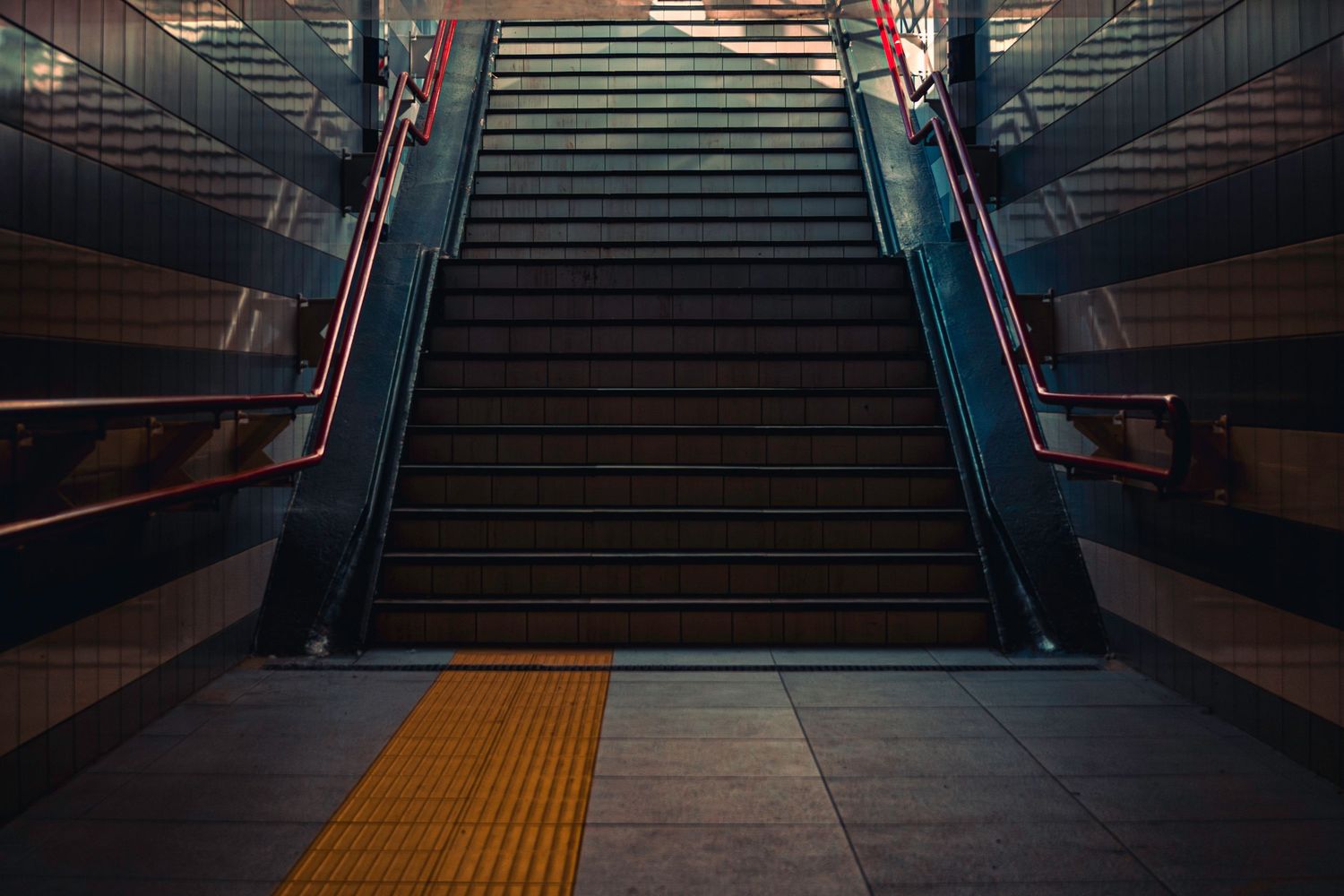 Dark empty train station escalator with yellow safety strip illuminated by ambient lighting.