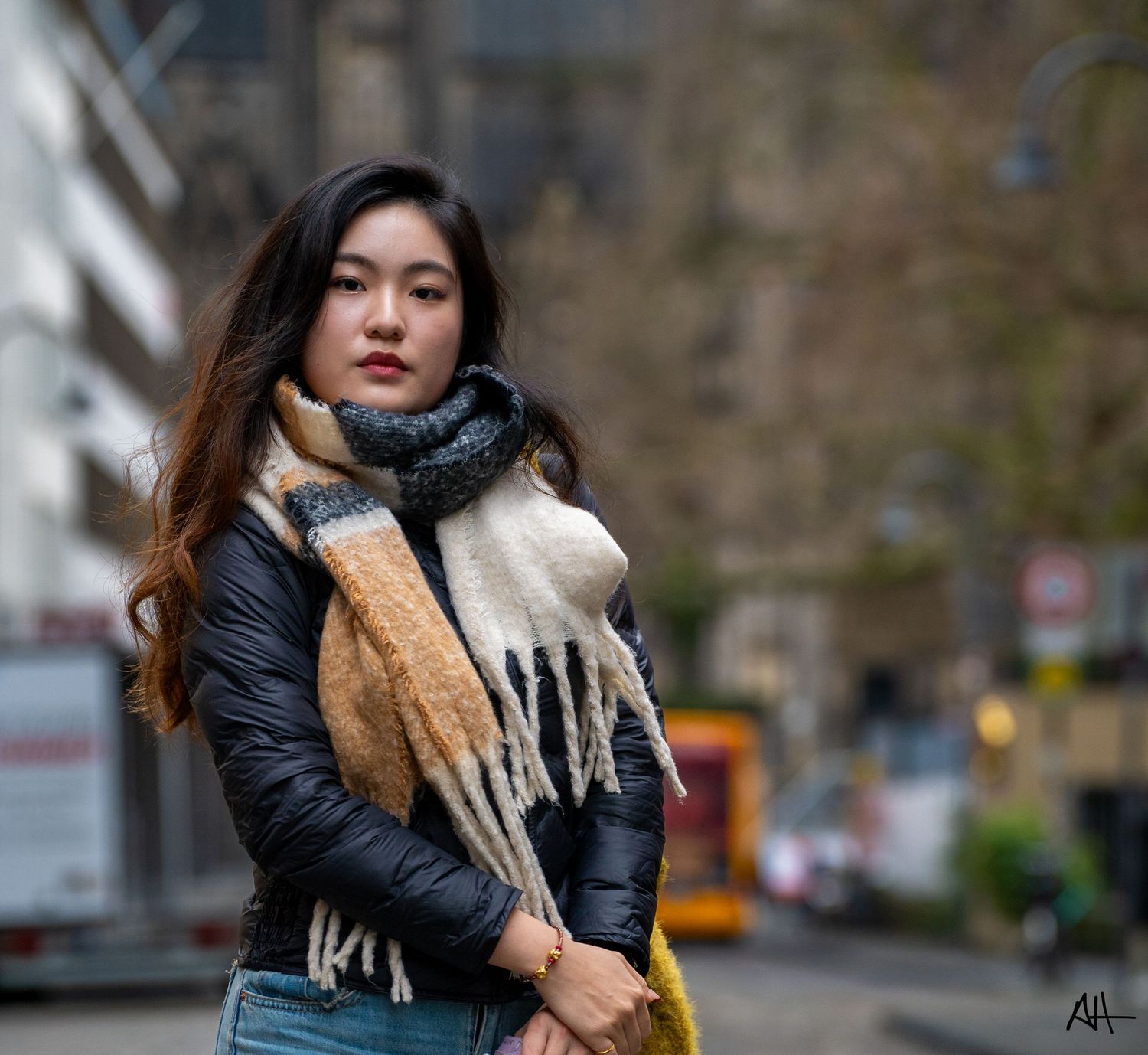 Outdoor portrait of a woman wearing a jacket and scarf, photographed on a city street.
