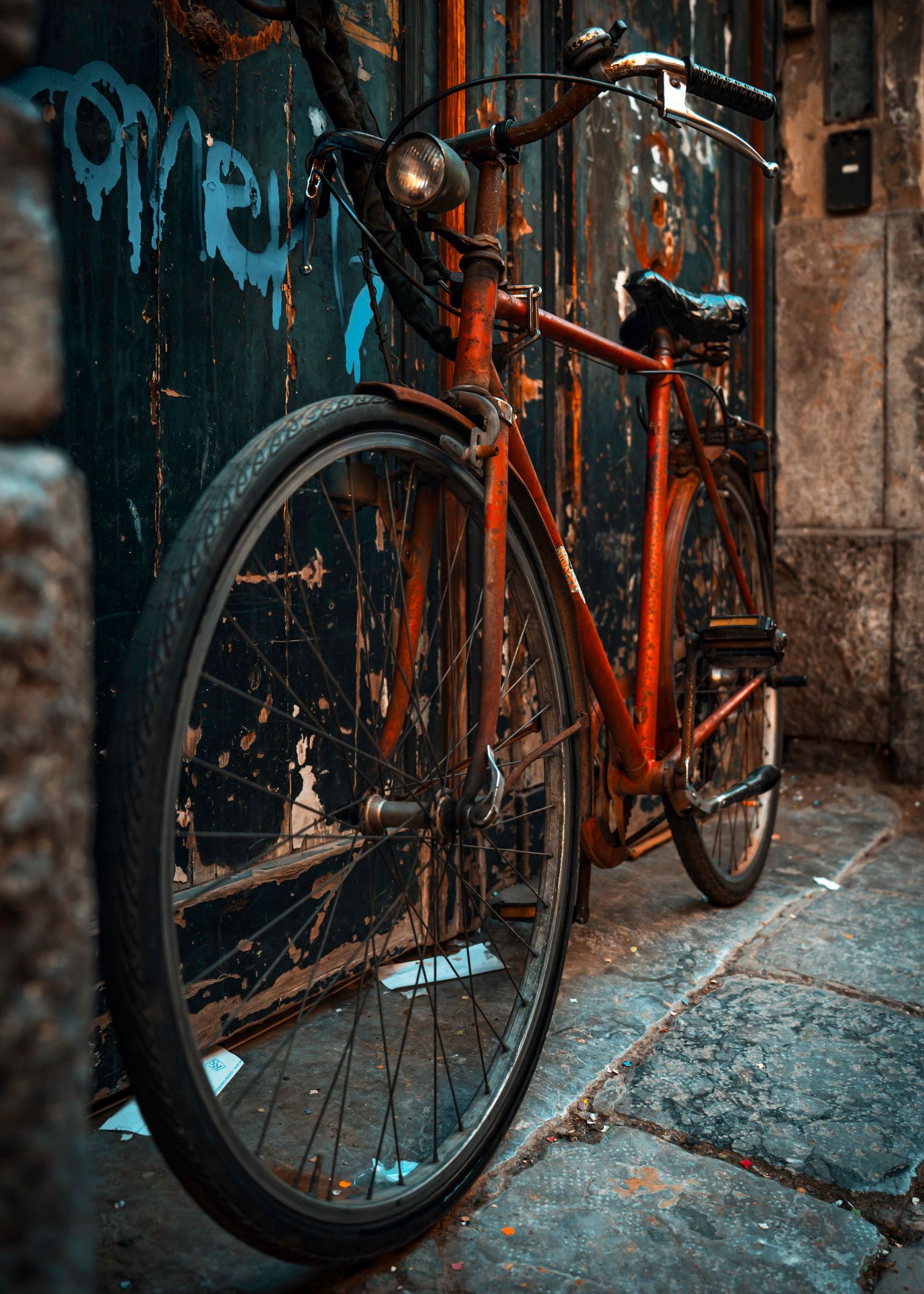 A vintage orange bicycle with thin tires leans against a weathered wall in moody lighting.