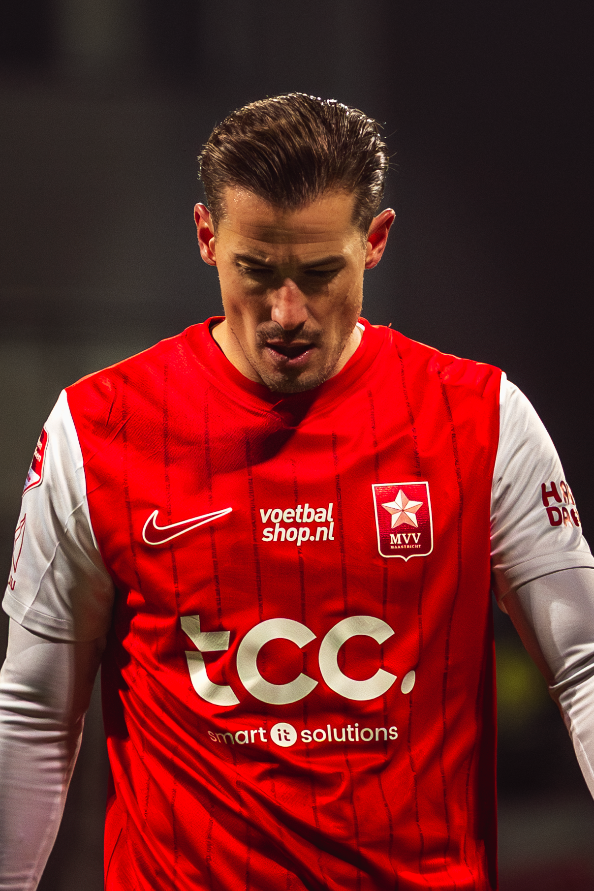 Soccer player in red and white jersey with TCC sponsor logo looking down during match.