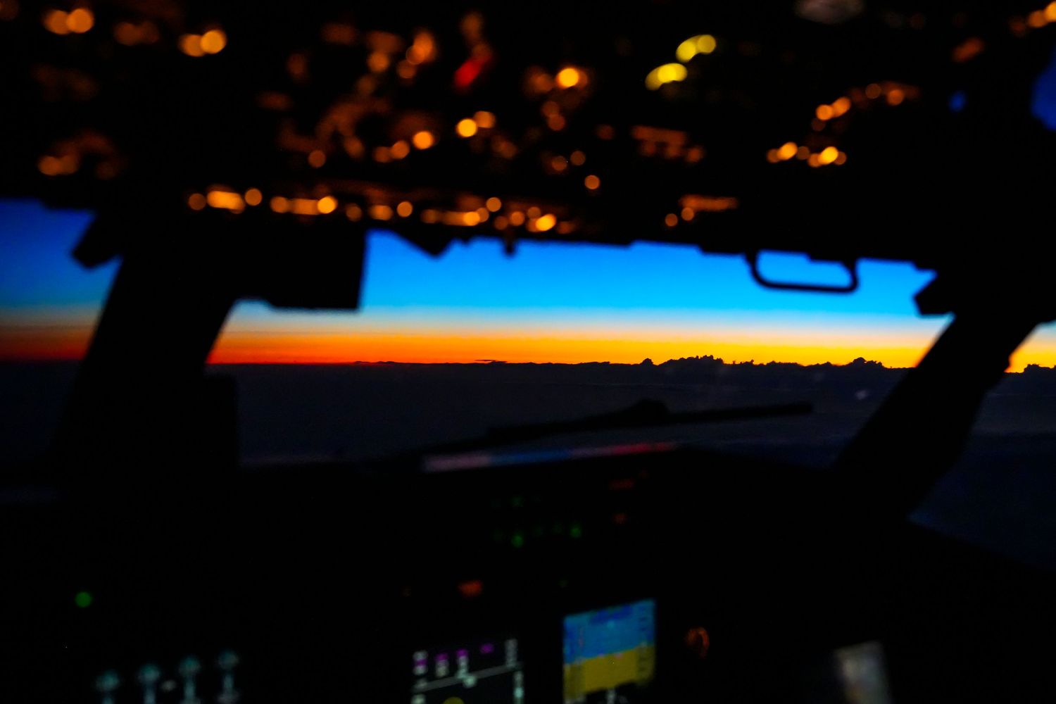 Scenic sunset view of an orange and blue sky through the cockpit windows, on board a NATO AWACS E-3A aircraft.