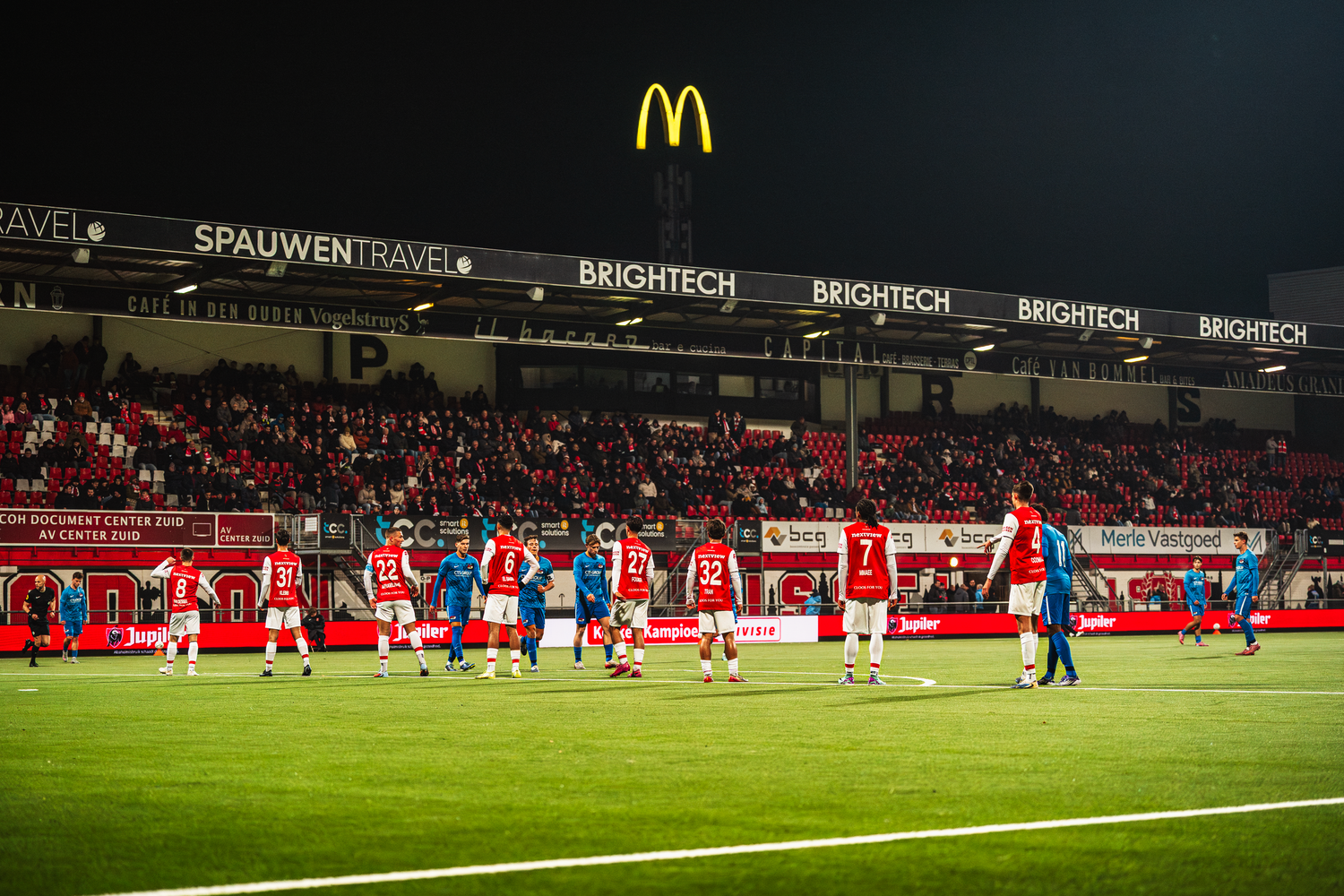 Soccer players line up on a field at night with McDonald's logo and stadium advertising boards visible in background.