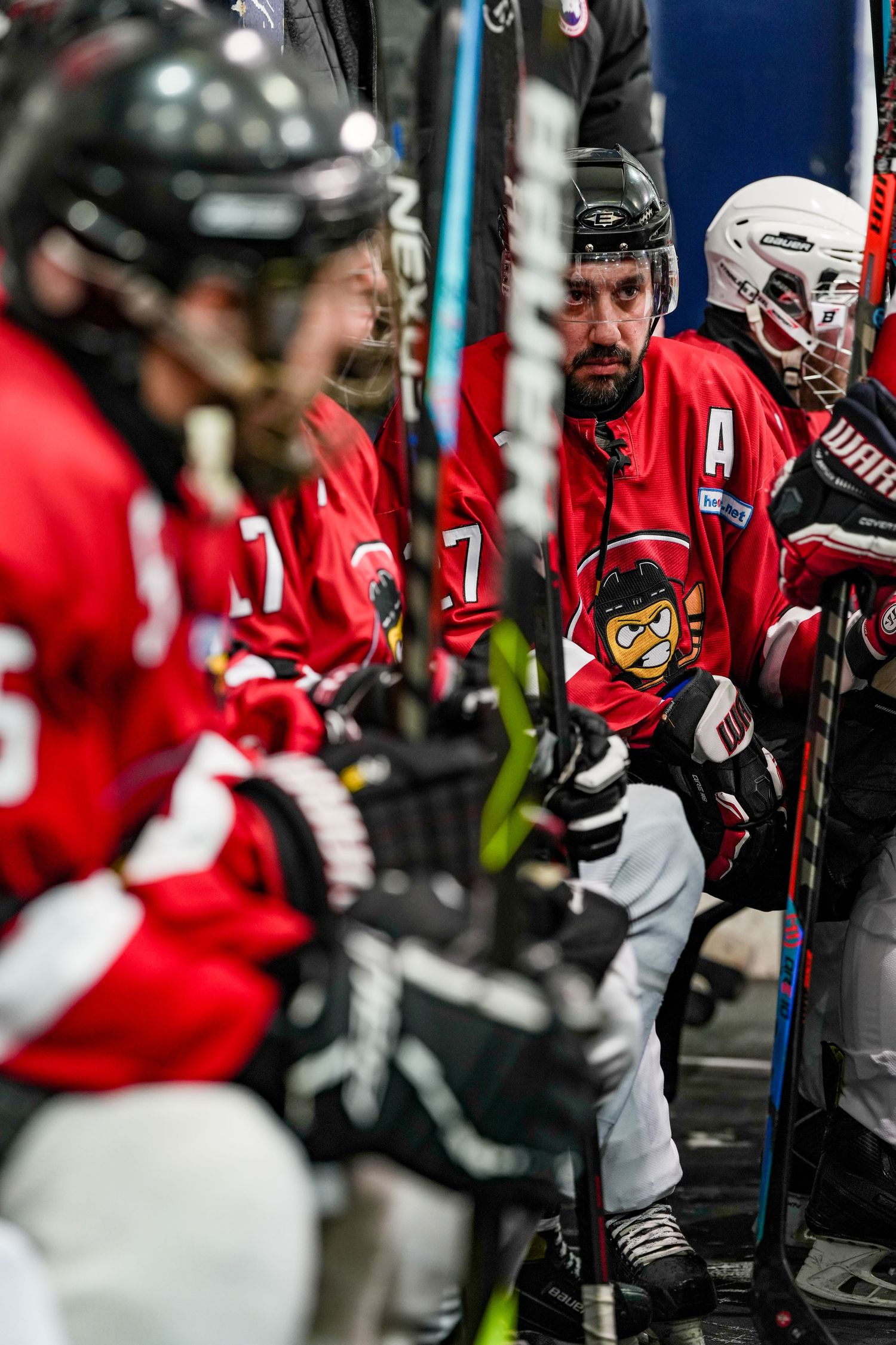Hockey players in red jerseys stand along the bench during a game, with their sticks resting on the boards.