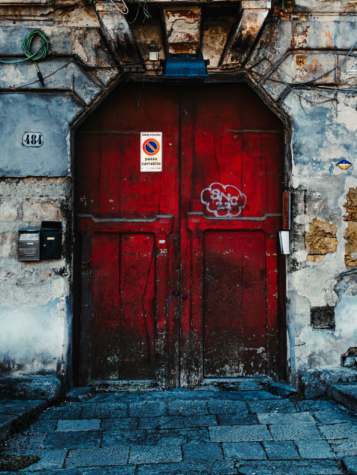 Vintage red doors with peeling paint and graffiti on weathered concrete walls create an urban industrial scene.