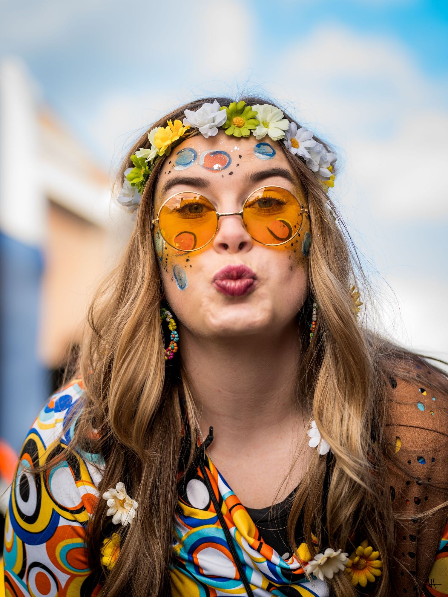 Colorful portrait of a woman wearing a flower crown and patterned clothing, photographed outdoors.