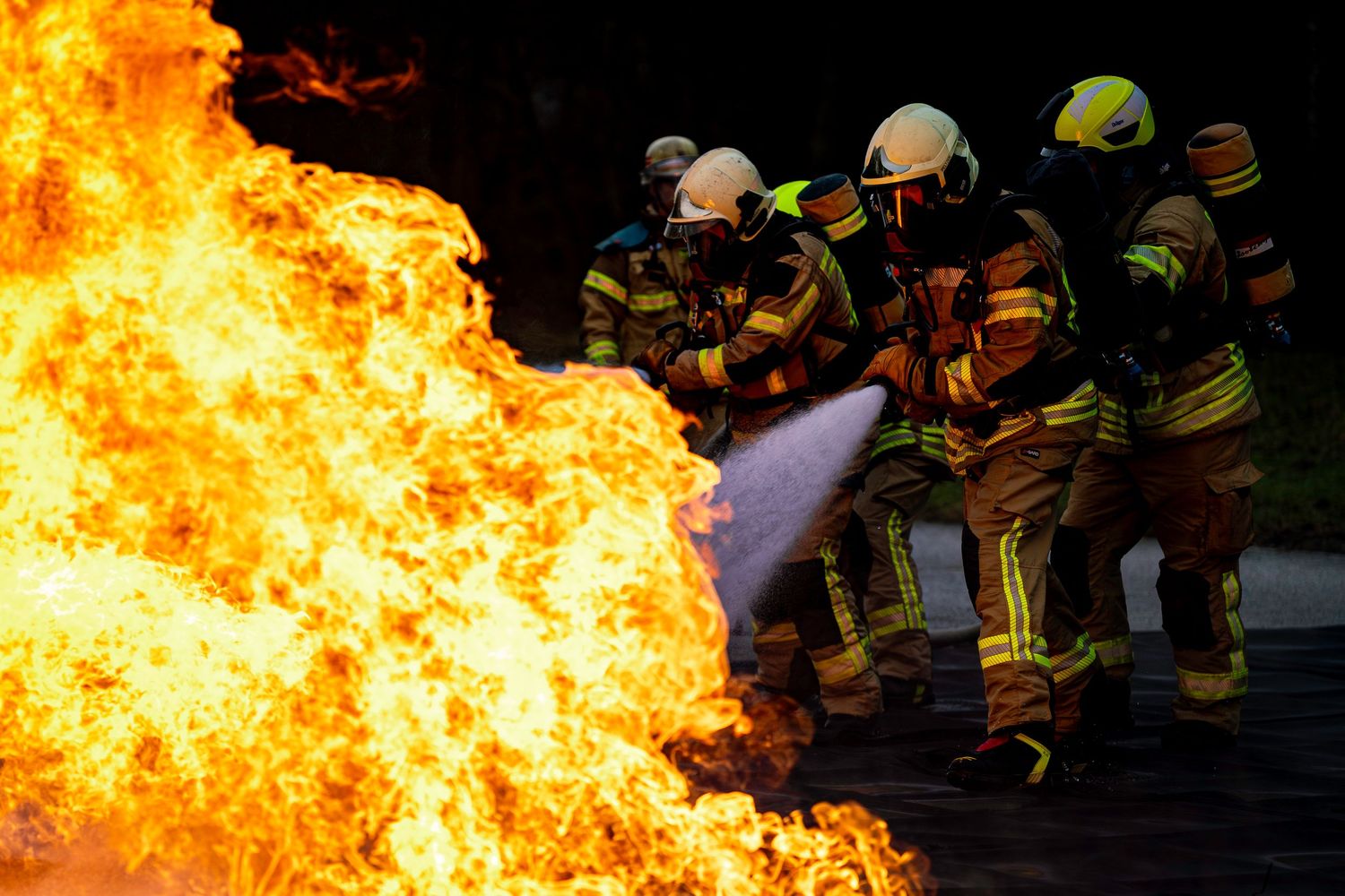 Firefighters in protective gear stand near intense orange flames during an emergency response training exercise.