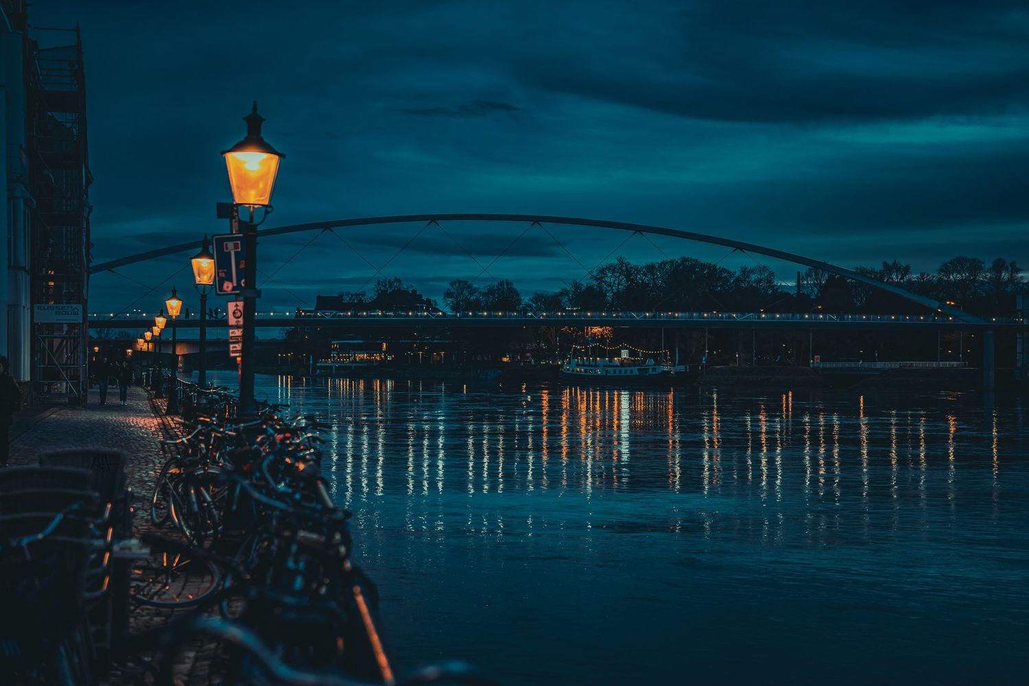 Nighttime photograph of a river and bridge in Maastricht illuminated by city lights.
