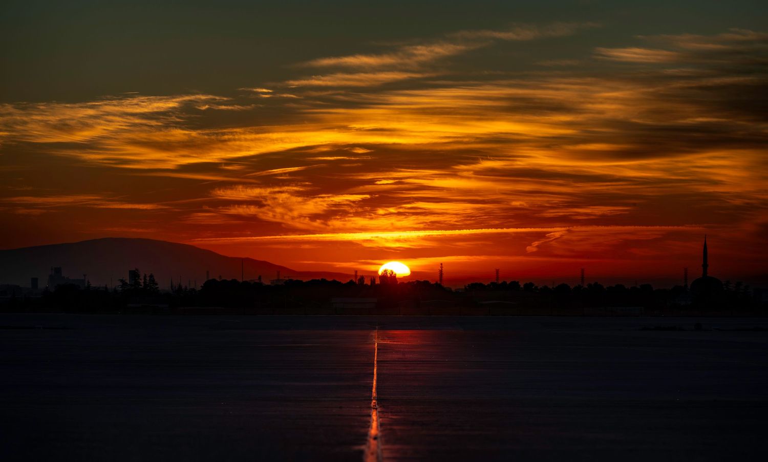 Dramatic orange sunrise over creates silhouettes of mountains, mosques and buildings against a fiery sky.