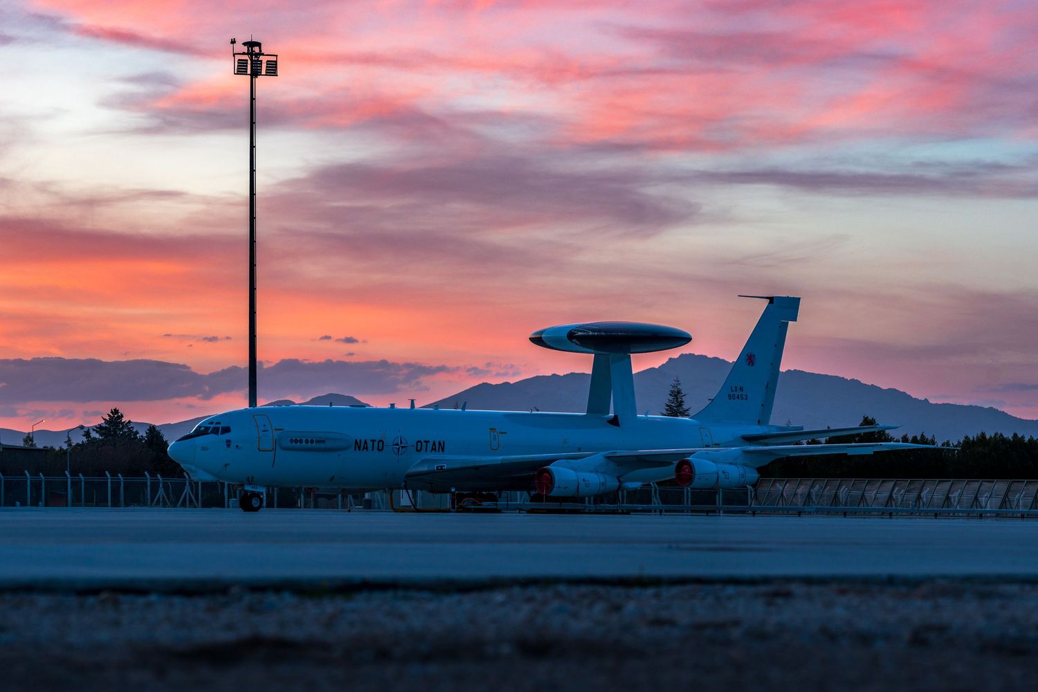 Military surveillance aircraft silhouetted against a dramatic pink and orange sunset sky.