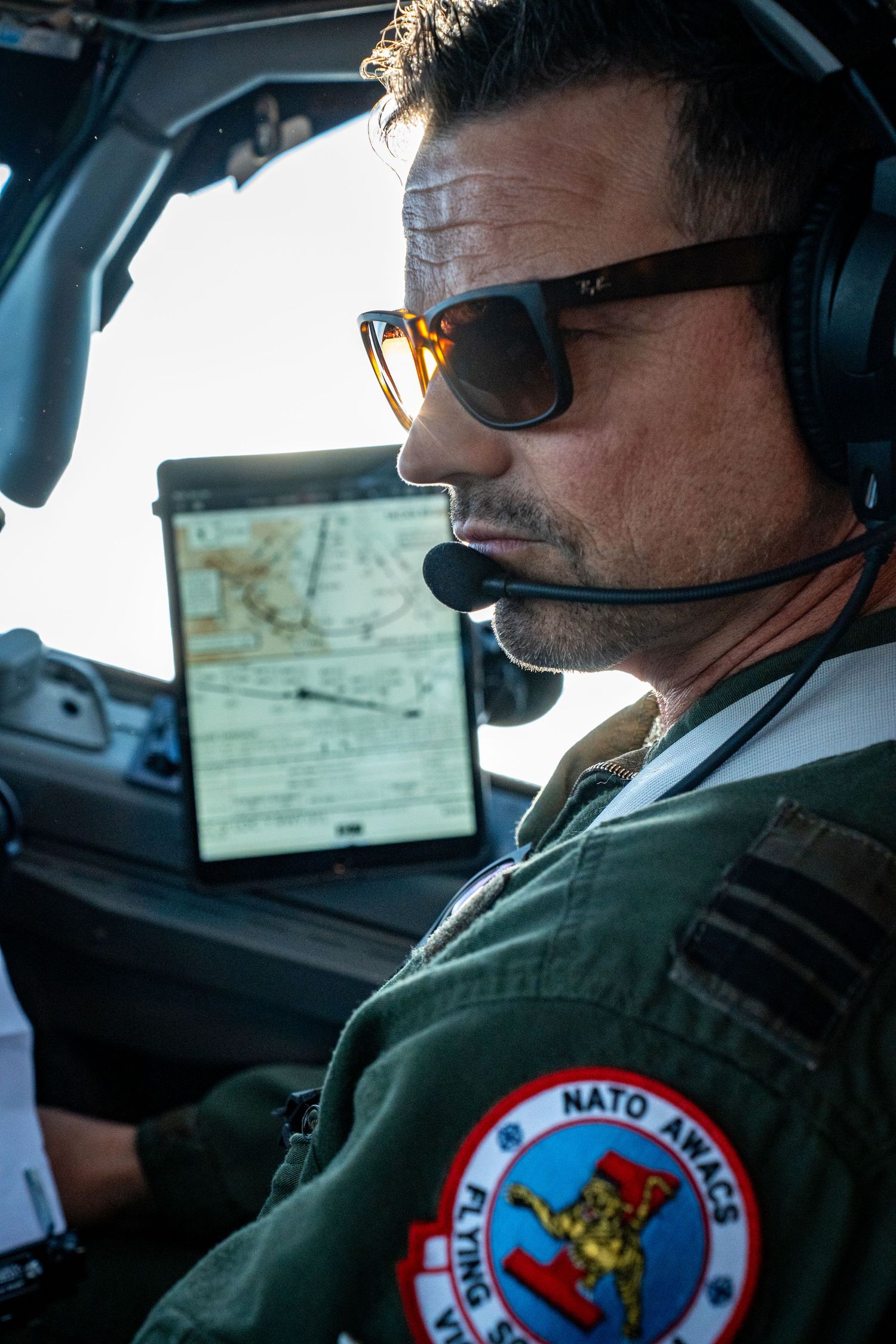 NATO AWACS pilot seated in the cockpit discussing mission details with another pilot.