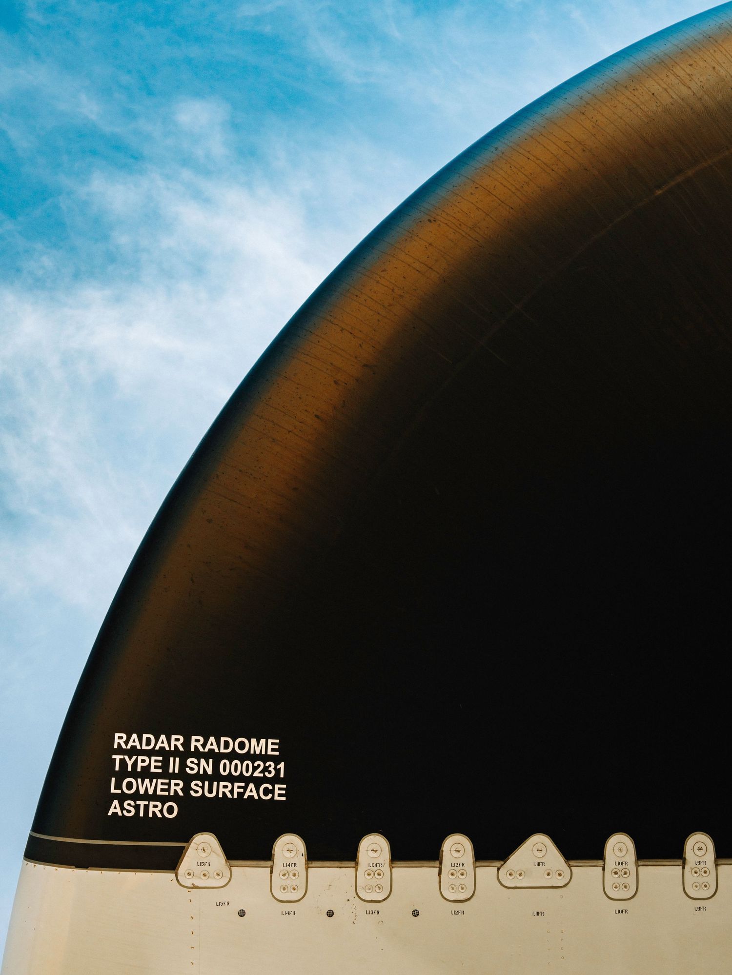 Close-up view of a radar radome with type identification text and rivets against a blue sky background.