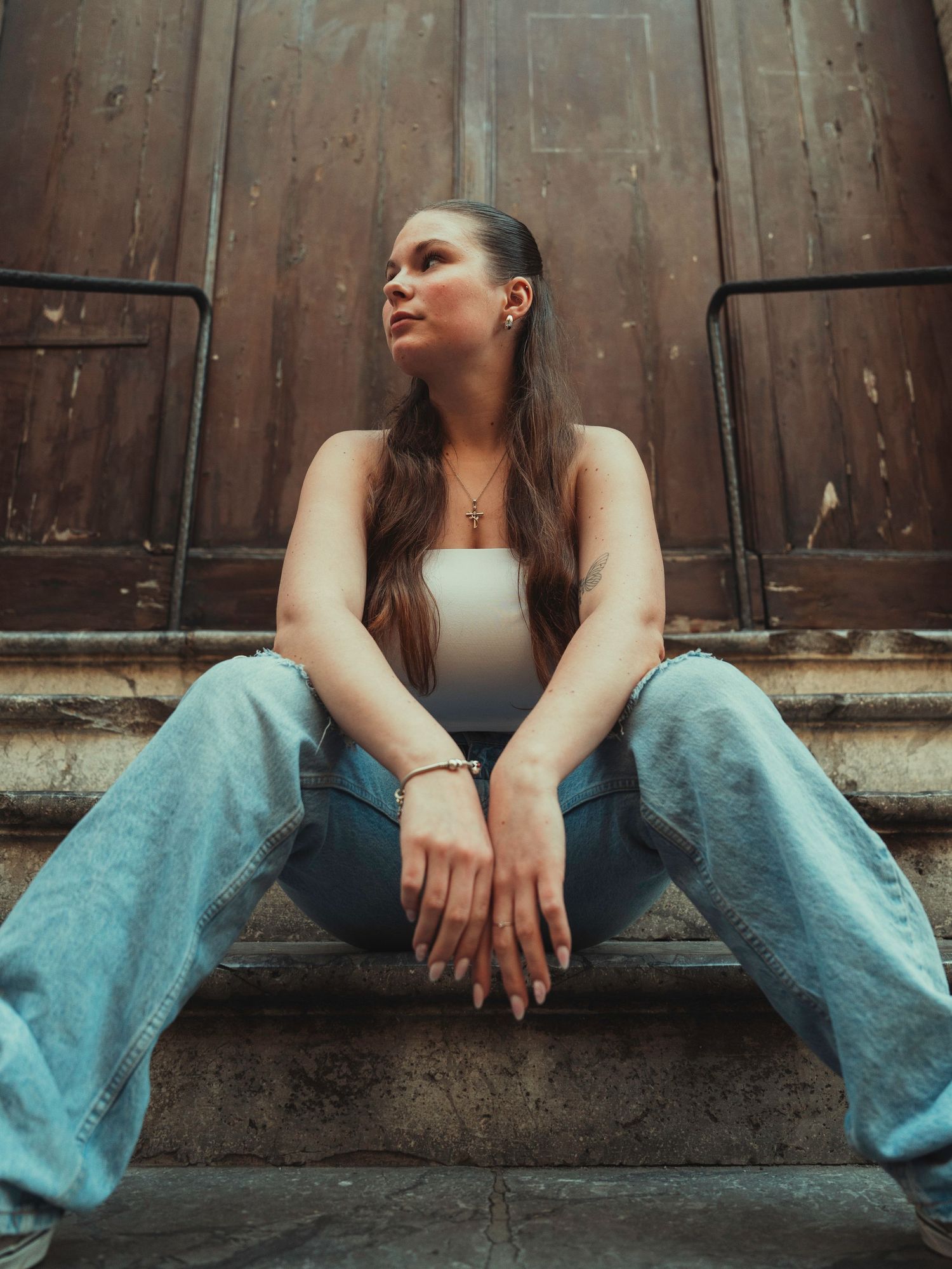 Person in light blue jeans sits against rustic wooden door in artistic portrait series.