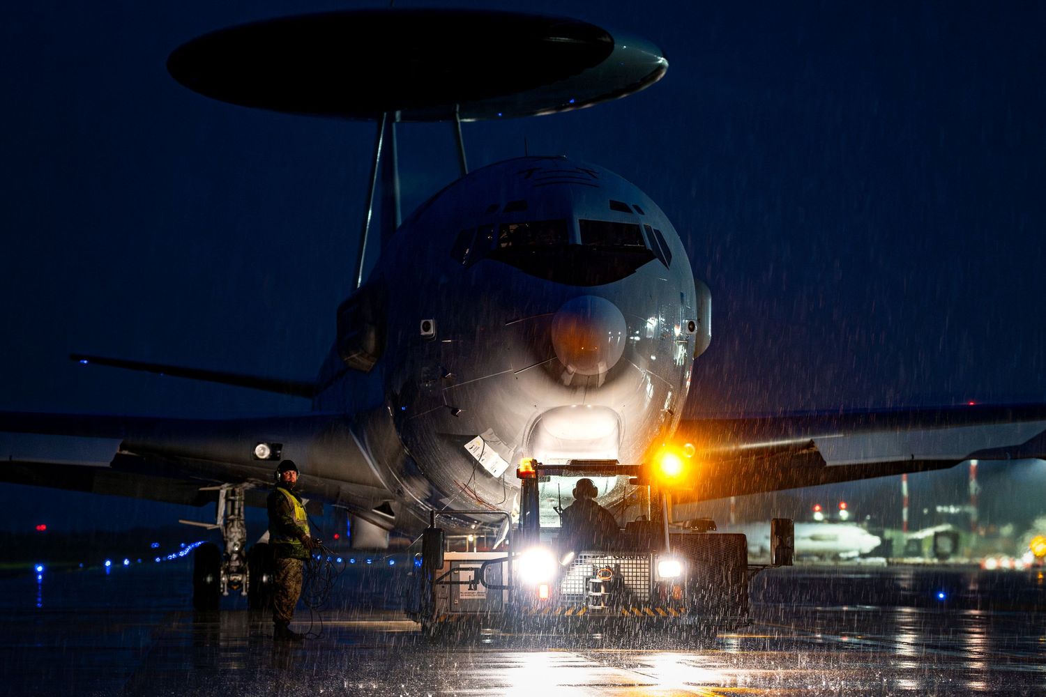 Aircraft being towed to the taxiway at night with multiple landing creating a dramatic atmosphere.