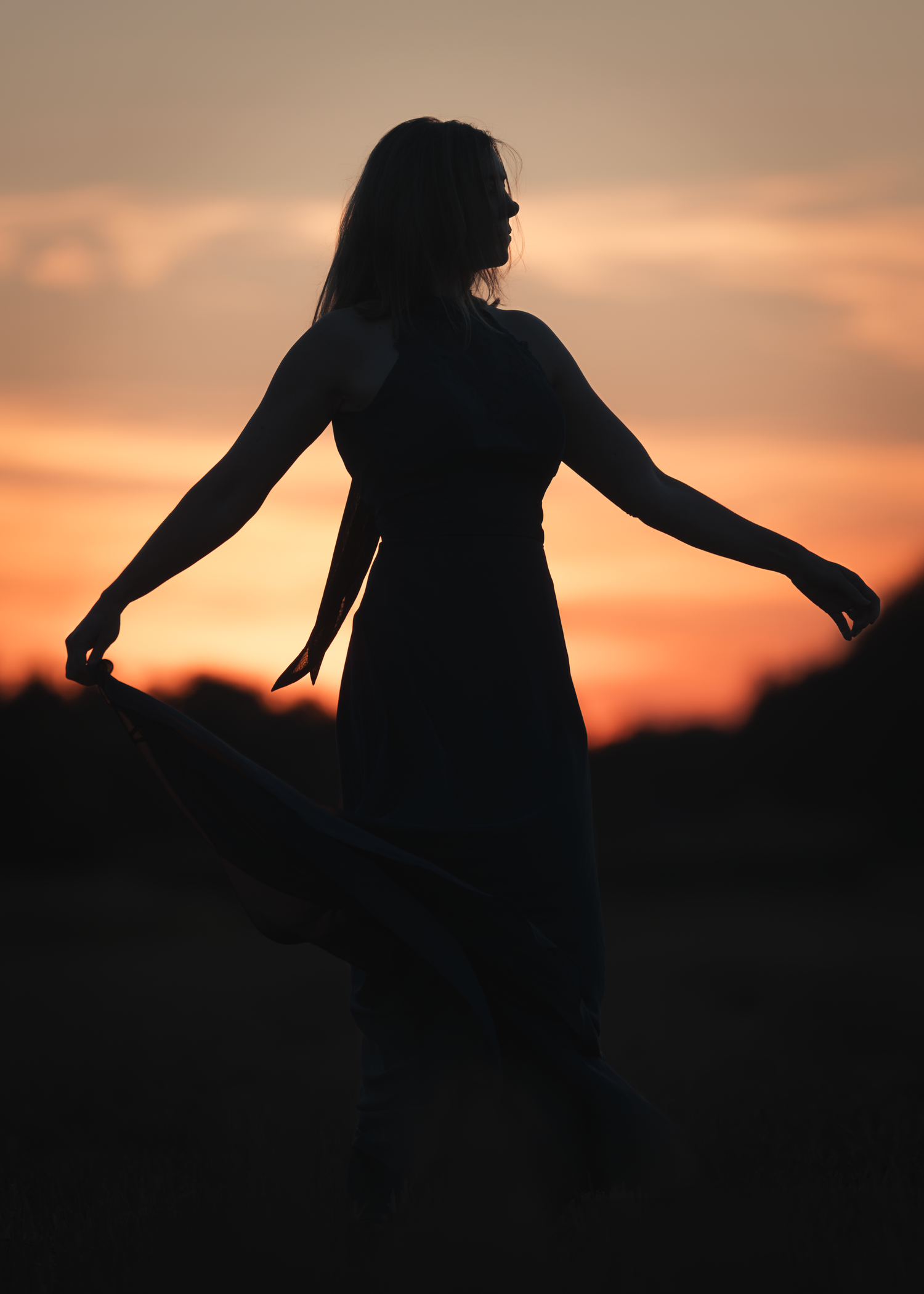 A silhouette of a person with arms outstretched stands against a vibrant orange sunset sky.
