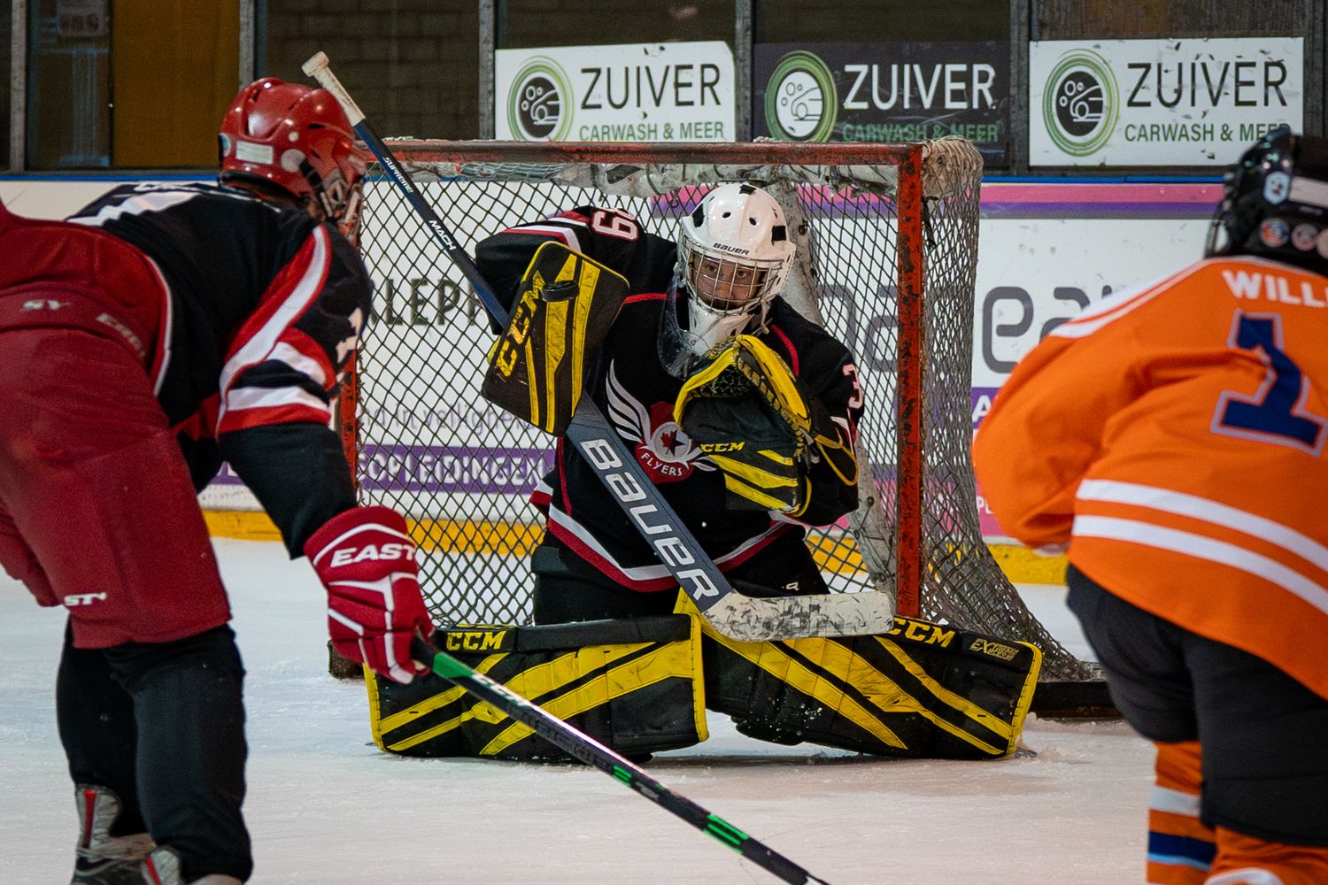 Hockey players in red, yellow, and orange jerseys compete for the puck during an intense ice hockey match.
